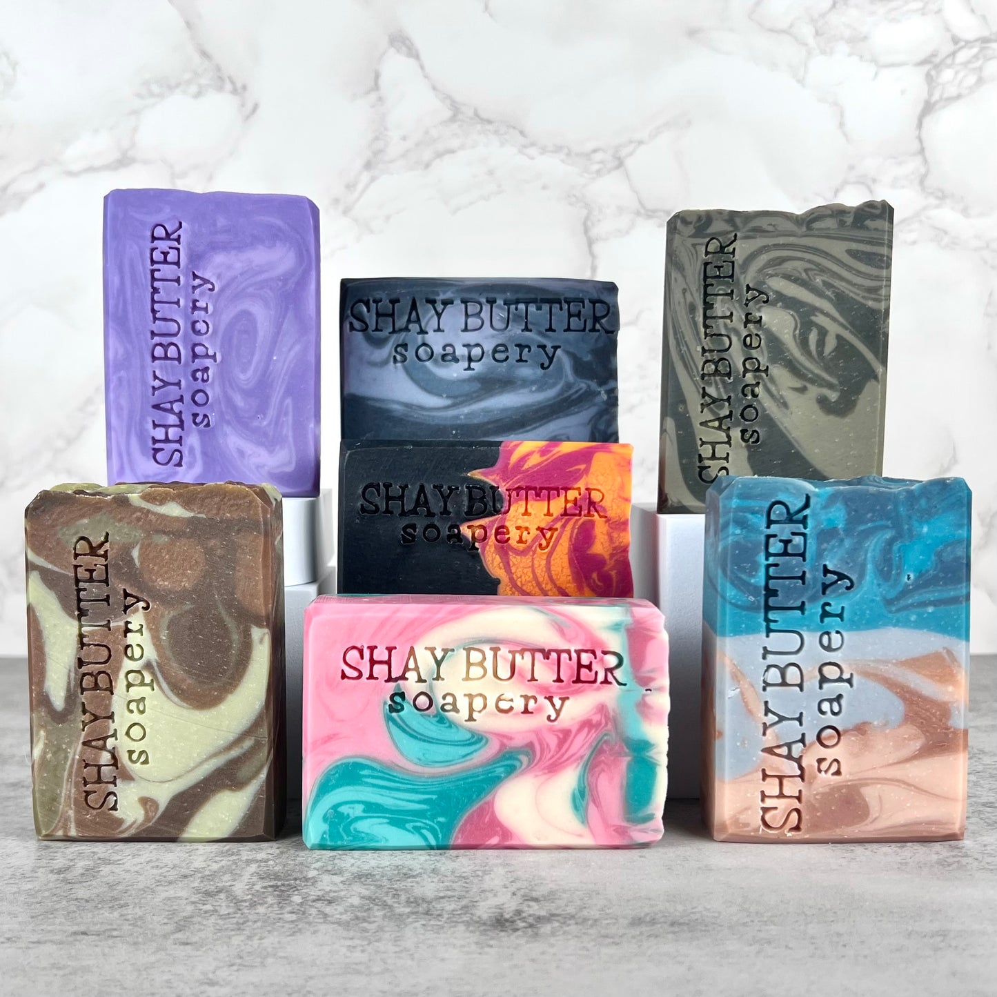 Assorted bars of Shay Butter Soapery on a marble surface with a white marble background