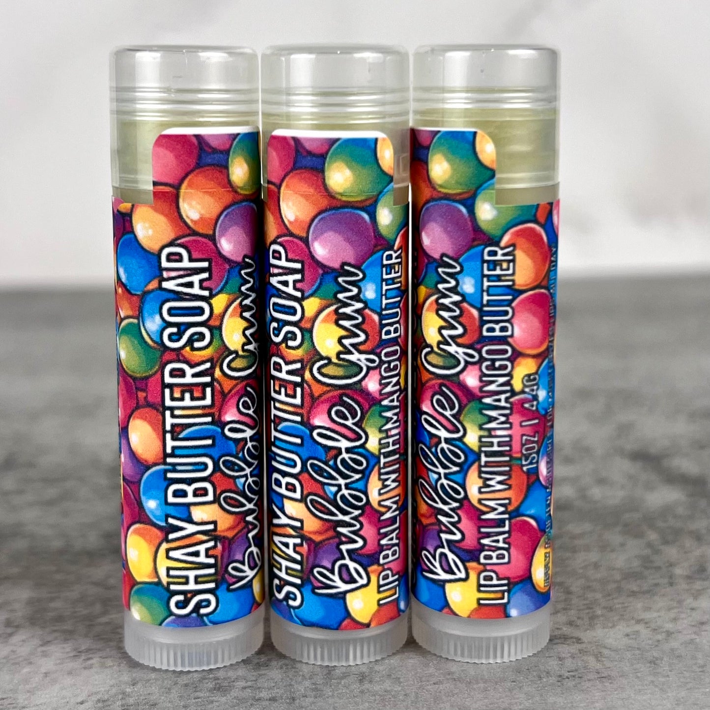 Three lip balm tubes with colorful packaging on a gray surface