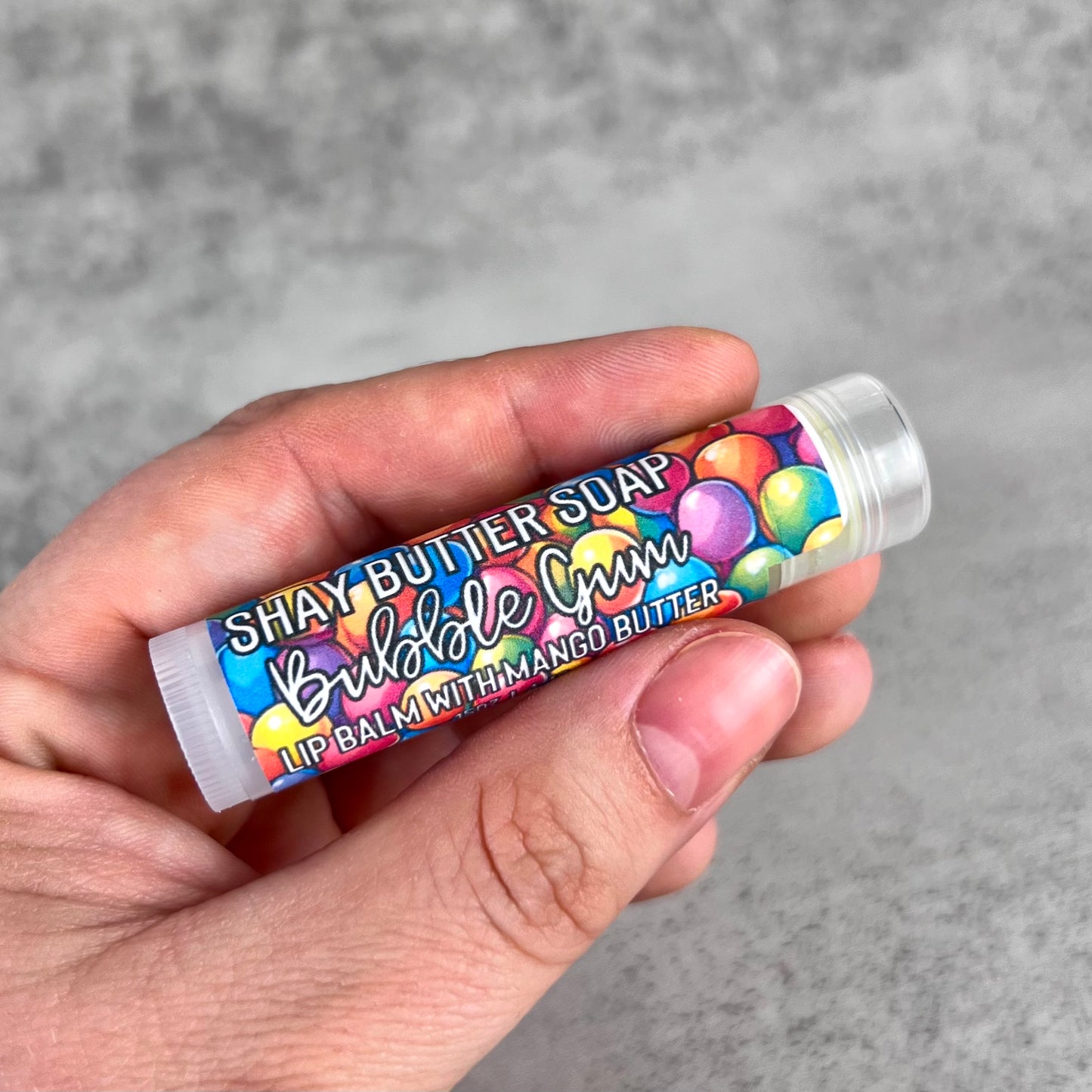 Hand holding a lip balm with colorful packaging against a gray background