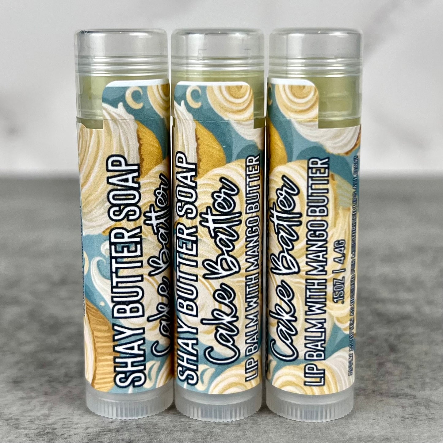 Three tubes of Cake Batter lip balm on a gray surface.