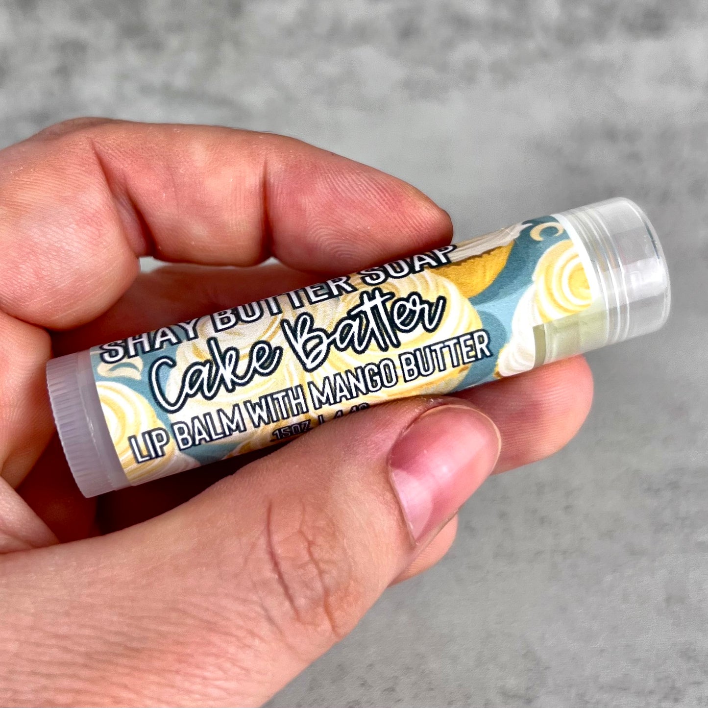 Lip balm with 'Shay Butter Soap' branding held in a hand against a gray background