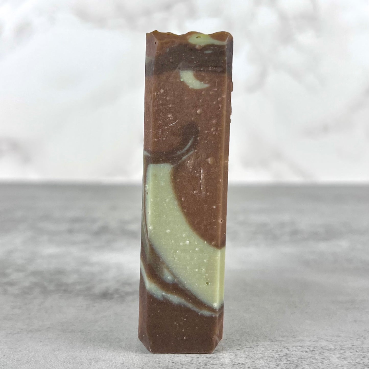 Marbled brown and green soap bar on a gray surface with a white background