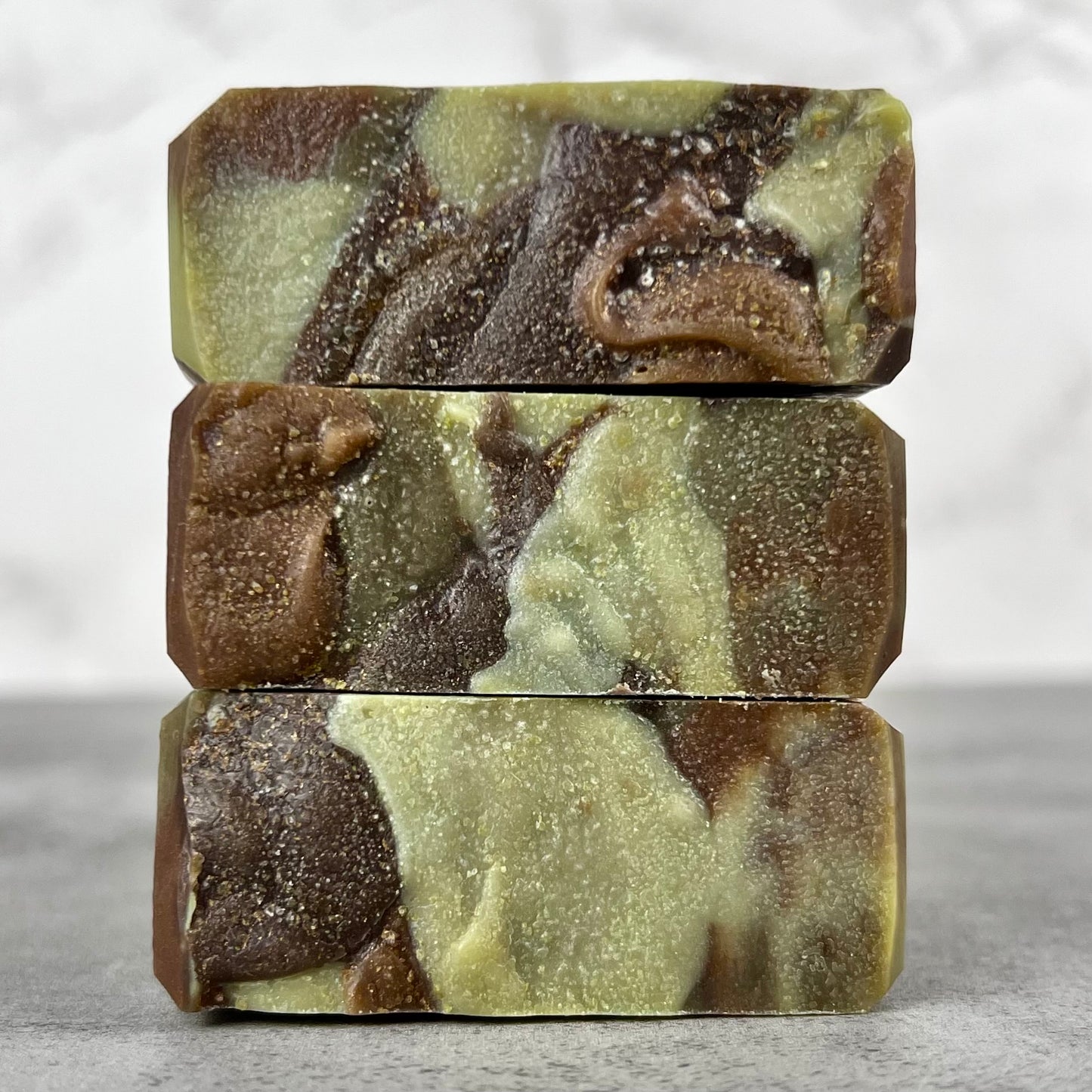 Stack of three green and brown marbled soap bars on a neutral background