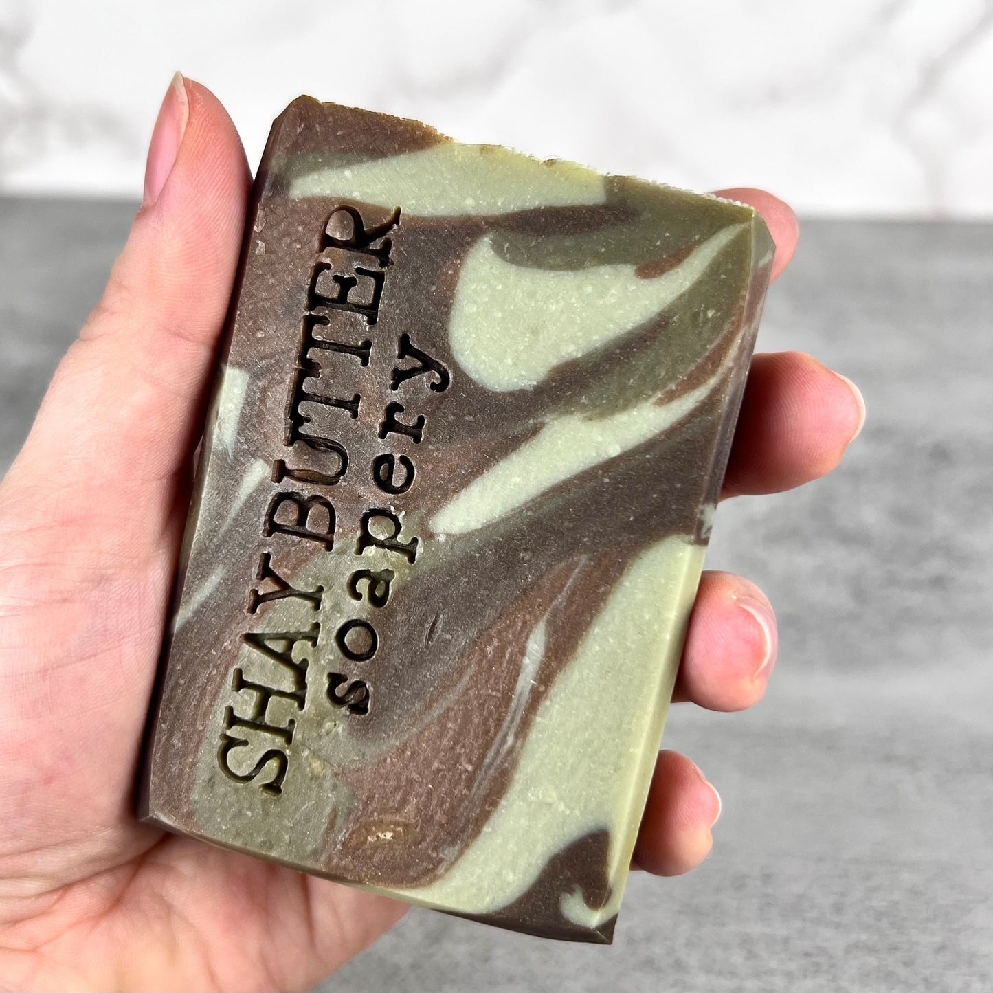 Hand holding a bar of soap with 'Shay Butter Soapery' branding.