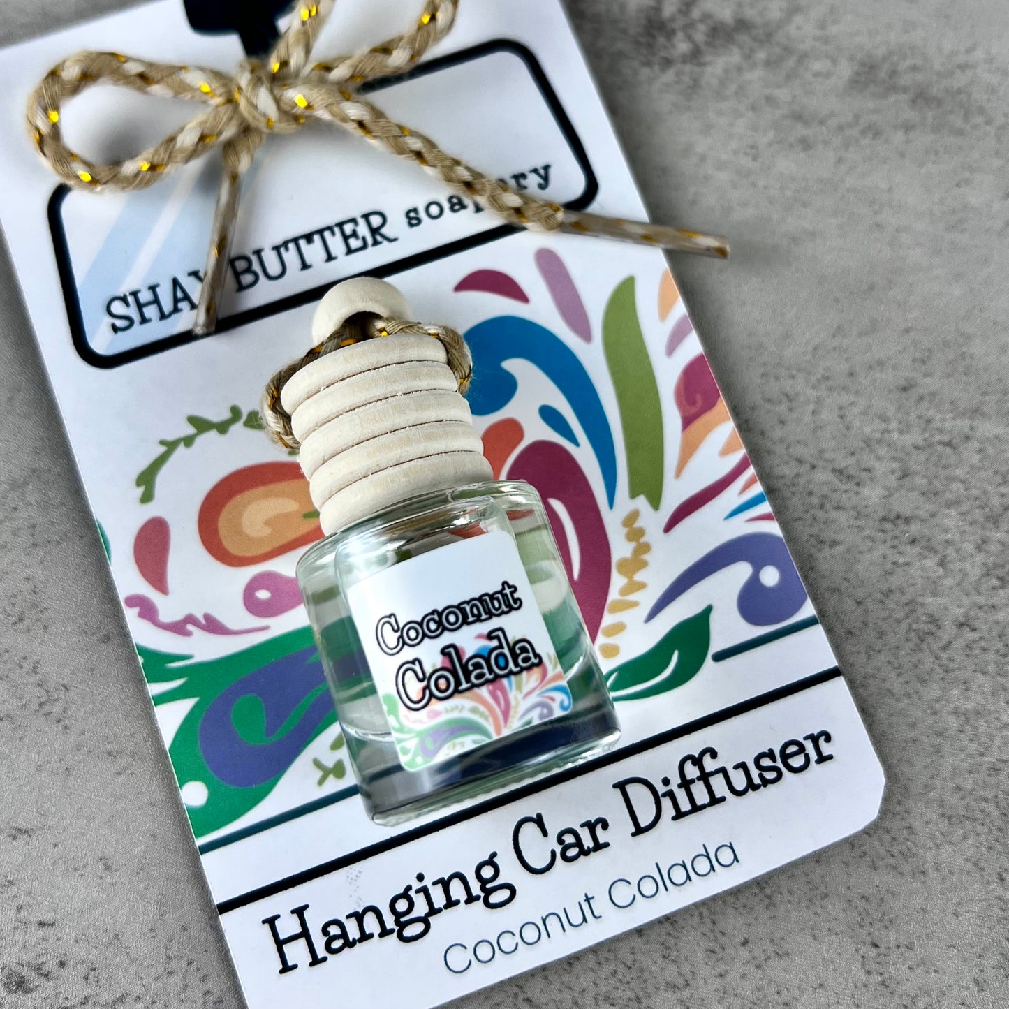 Coconut Colada hanging car diffuser with decorative packaging on a gray surface