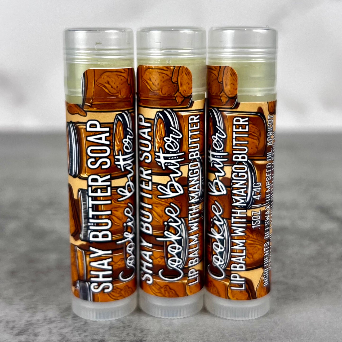 Three lip balm tubes on a gray surface.