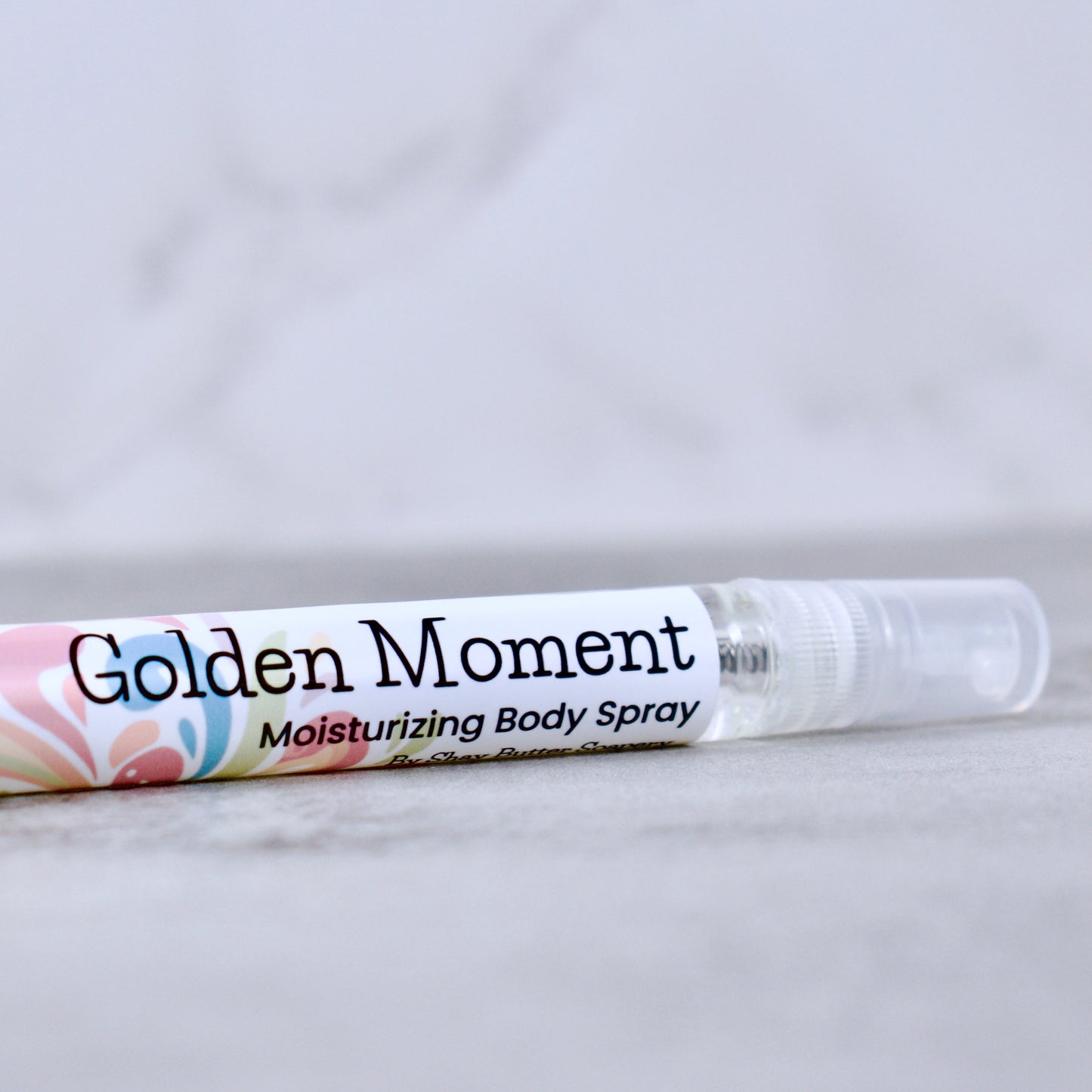 Golden Moment moisturizing body spray on a marble surface with a light gray background