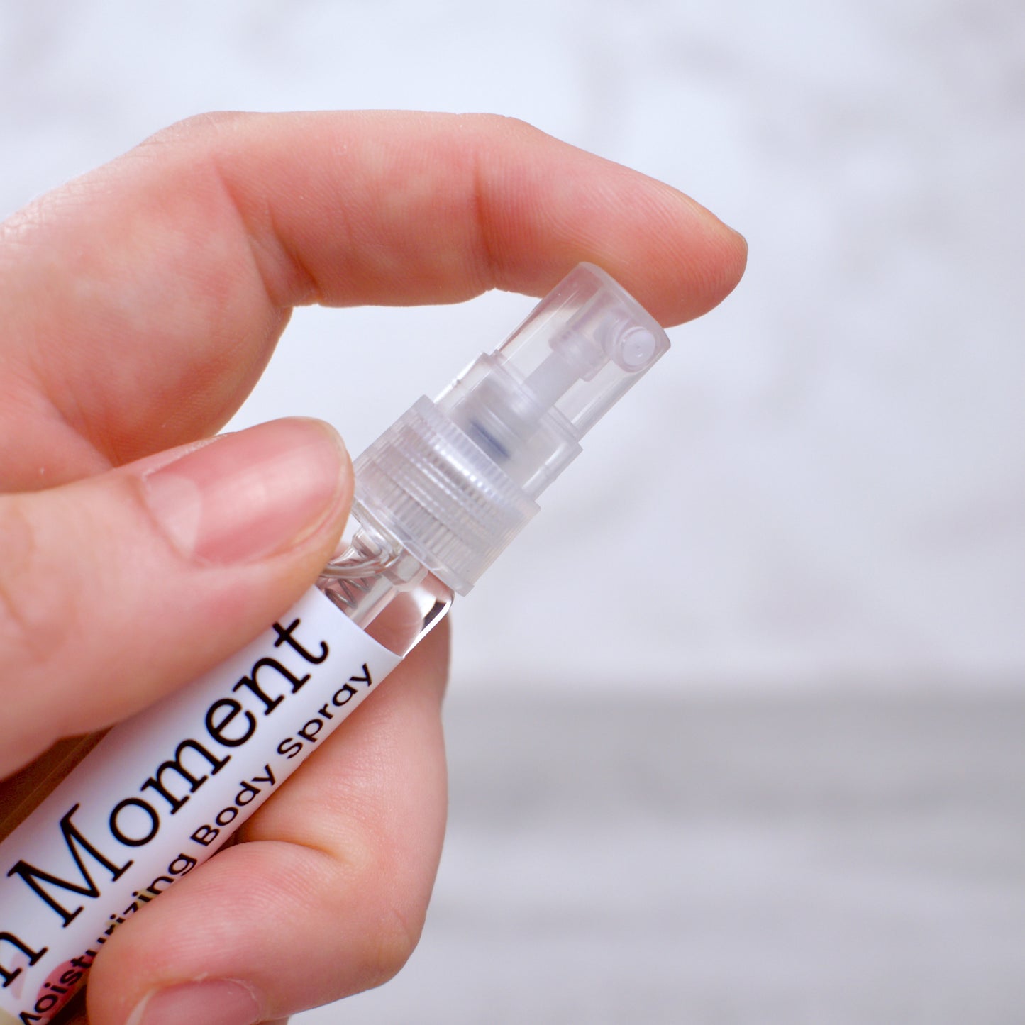 Hand holding a small spray bottle labeled 'Golden Moment' against a blurred background