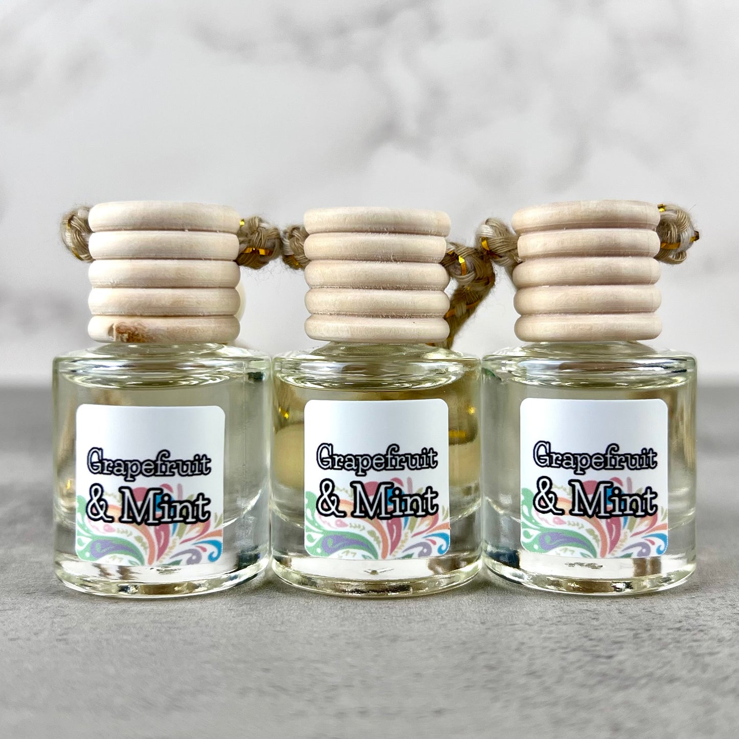 Three hanging car diffusers labeled 'Grapefruit & Mint' with wooden caps on a gray background.