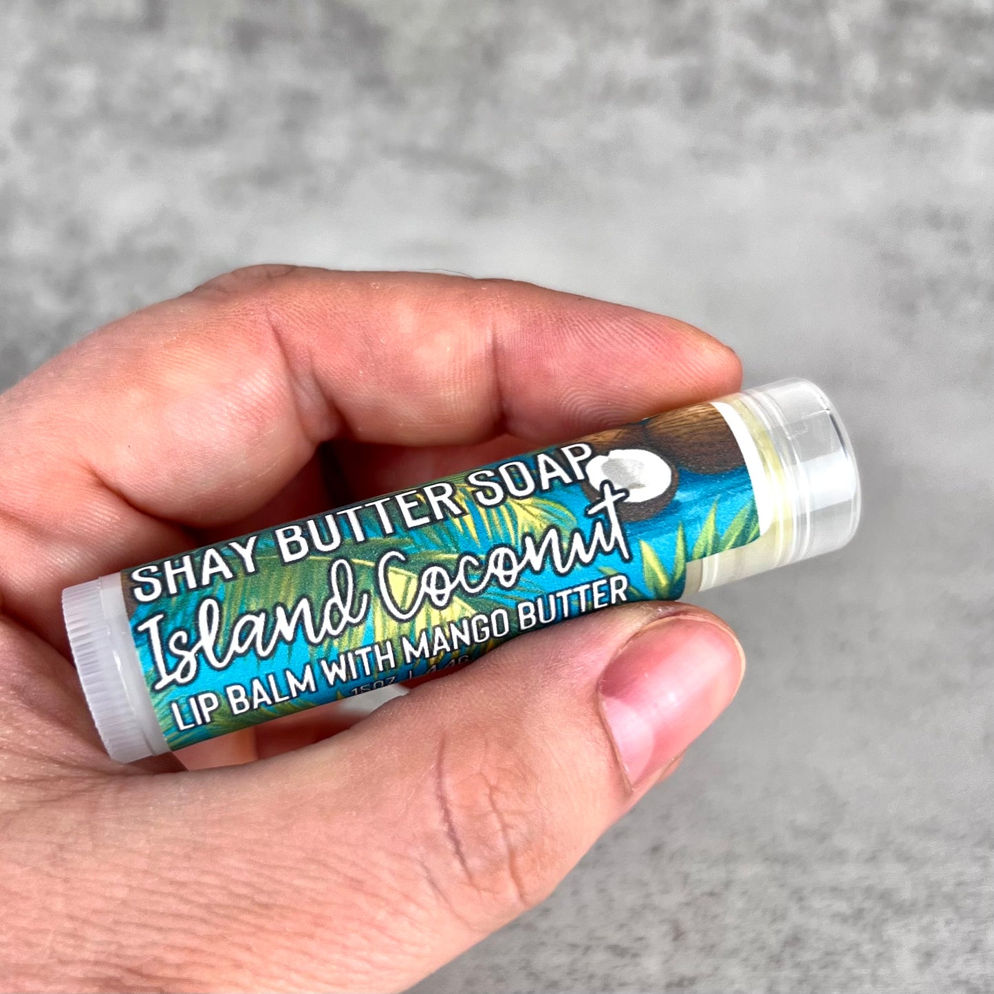 Lip balm with 'Shay Butter Soap' label held in a hand against a gray background