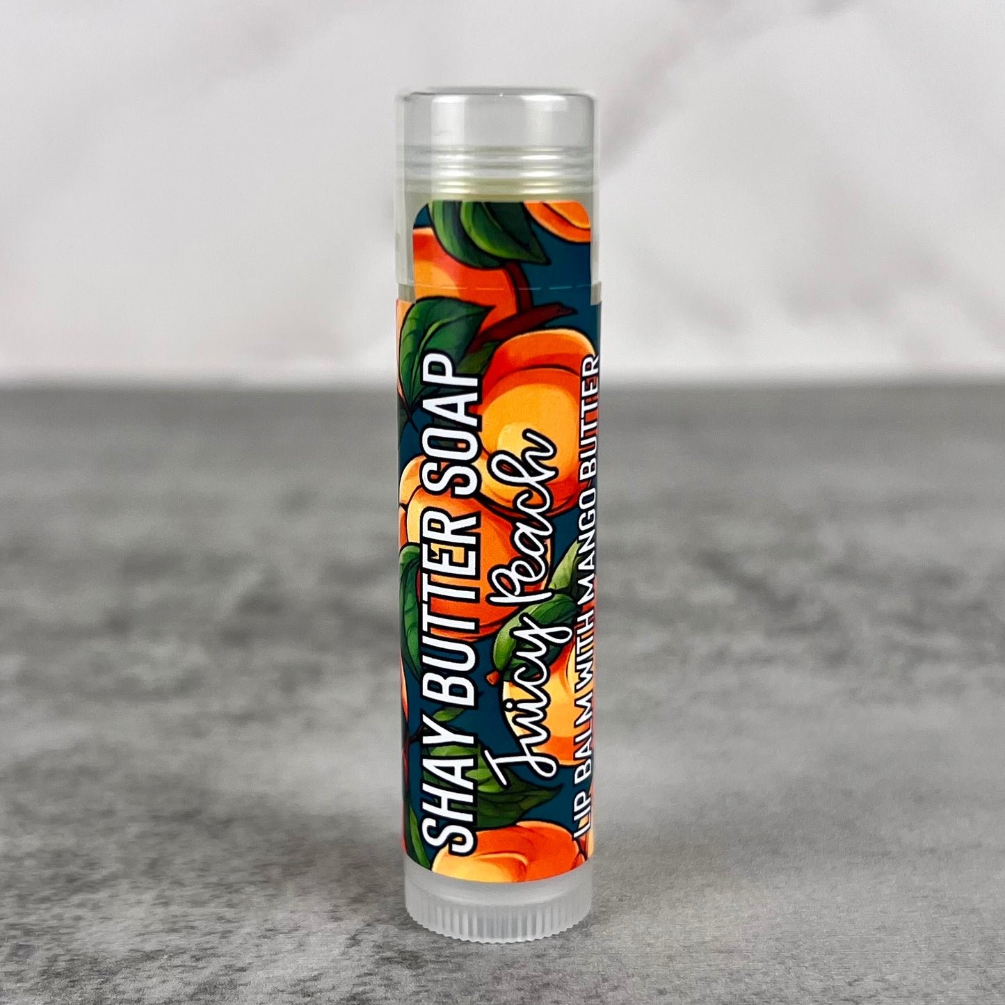 Shay Butter Soap Juicy Peach lip balm on a gray surface with a white background
