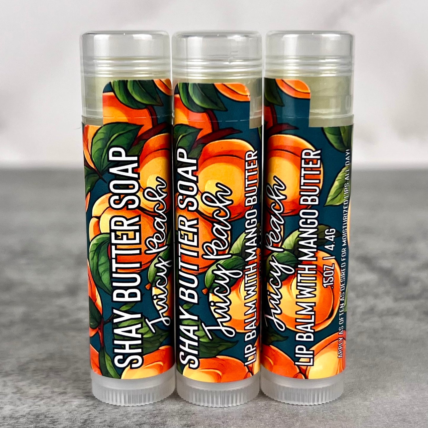 Juicy peach lip balm tubes on a gray surface.