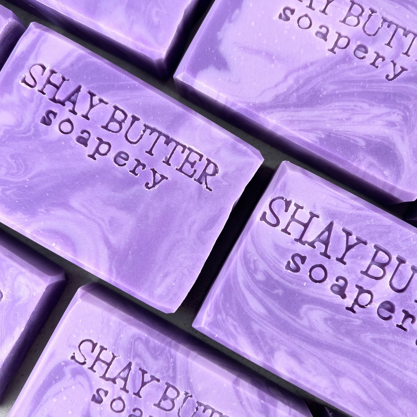 Close-up of purple soap bars with 'Shay Butter Soapery' branding.
