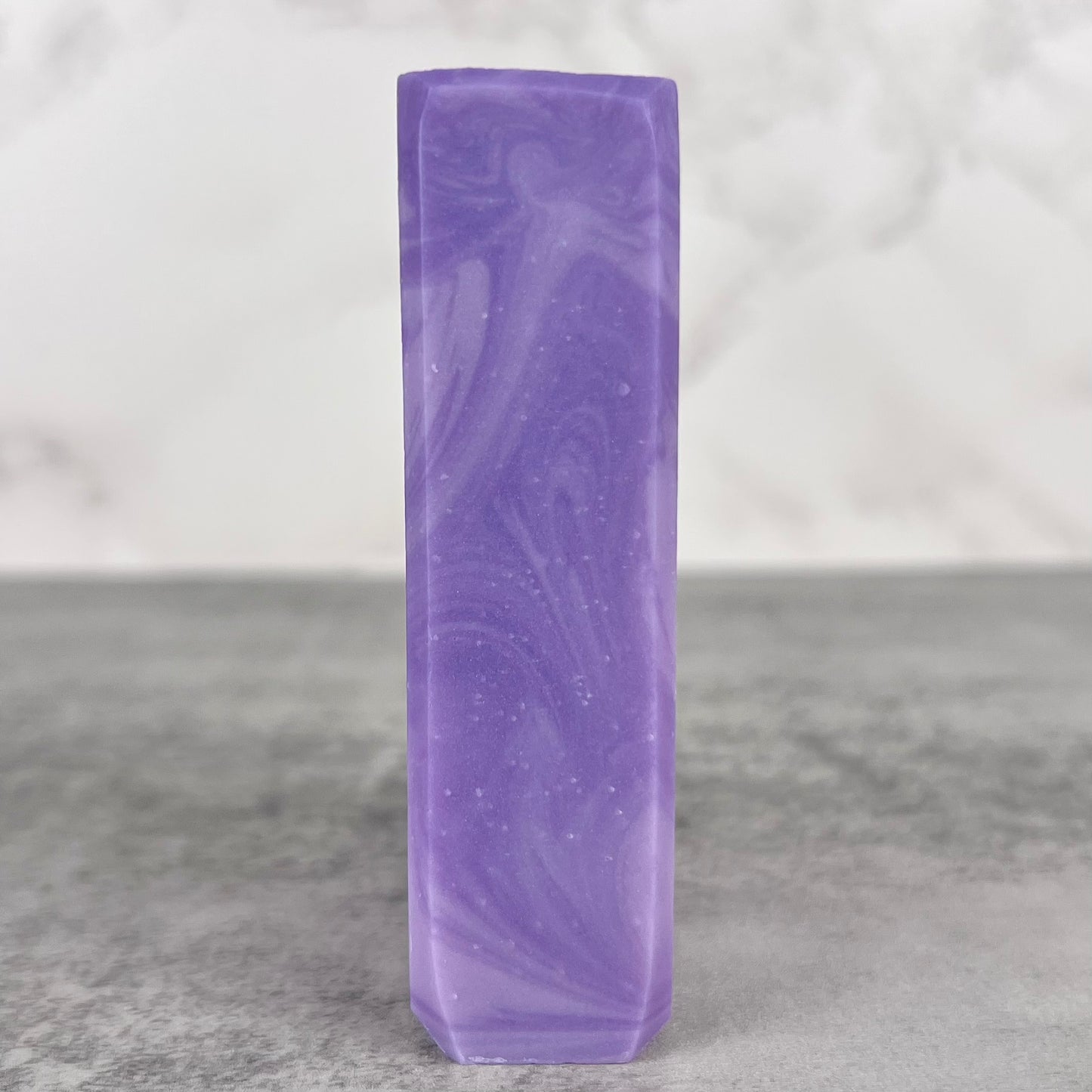 Purple marbled soap bar on a gray surface with a light gray background