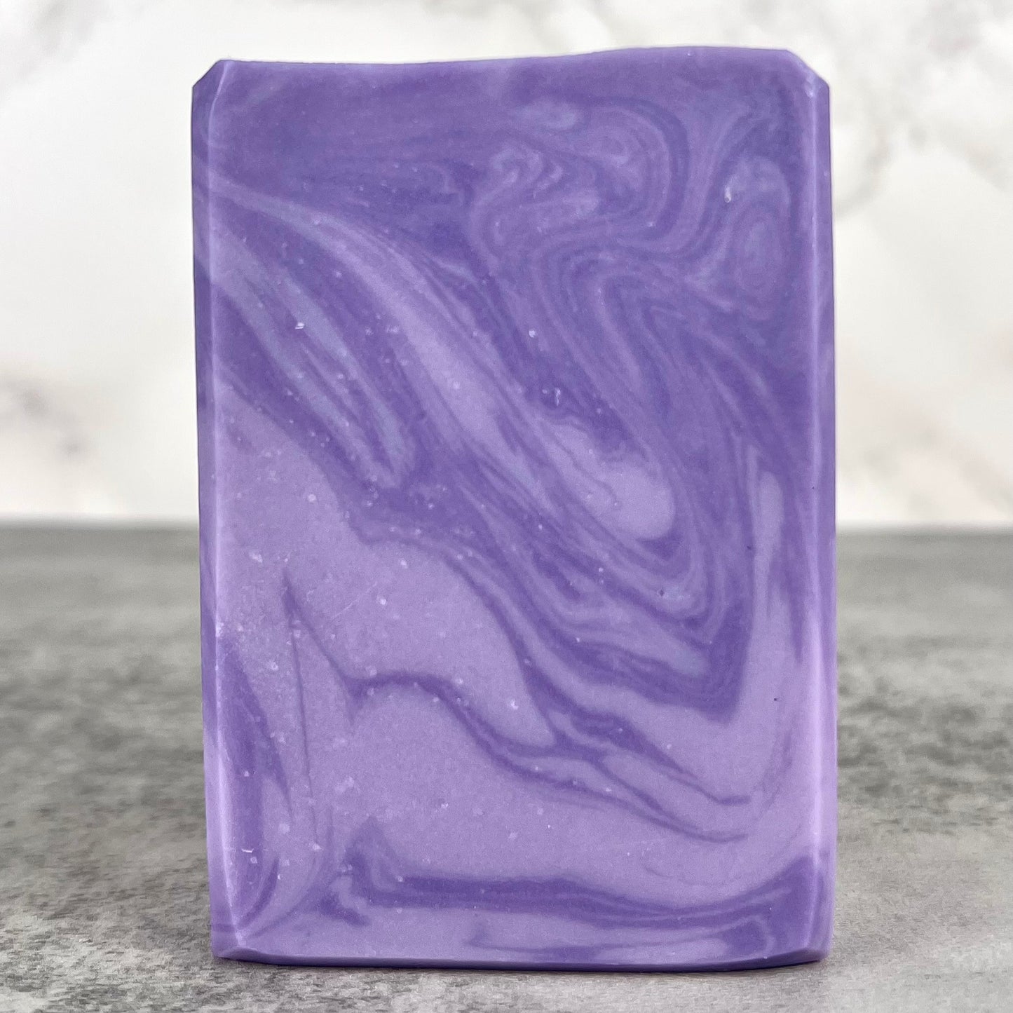 Purple marbled soap bar on a gray surface with a white background