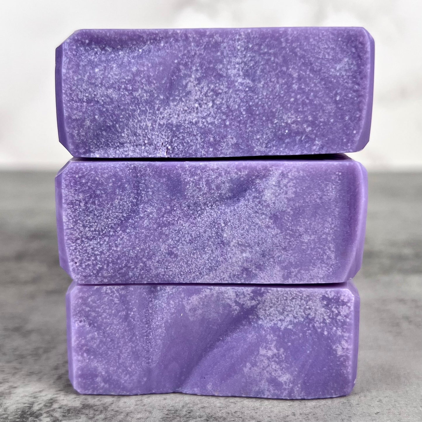 Three stacked purple soap bars on a gray surface with a neutral background