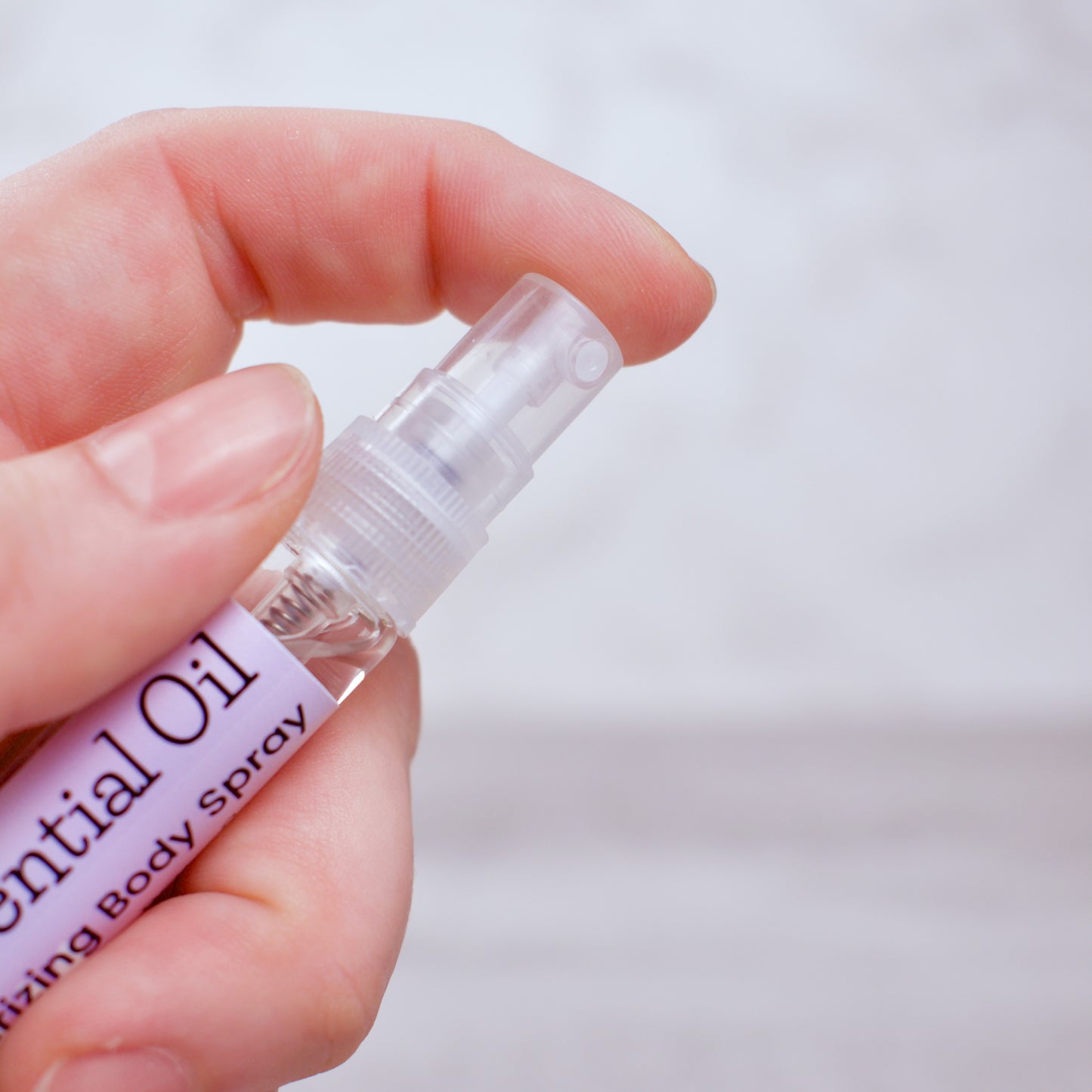 Hand holding a small bottle labeled 'Lavender Essential Oil Body Spray' against a light background