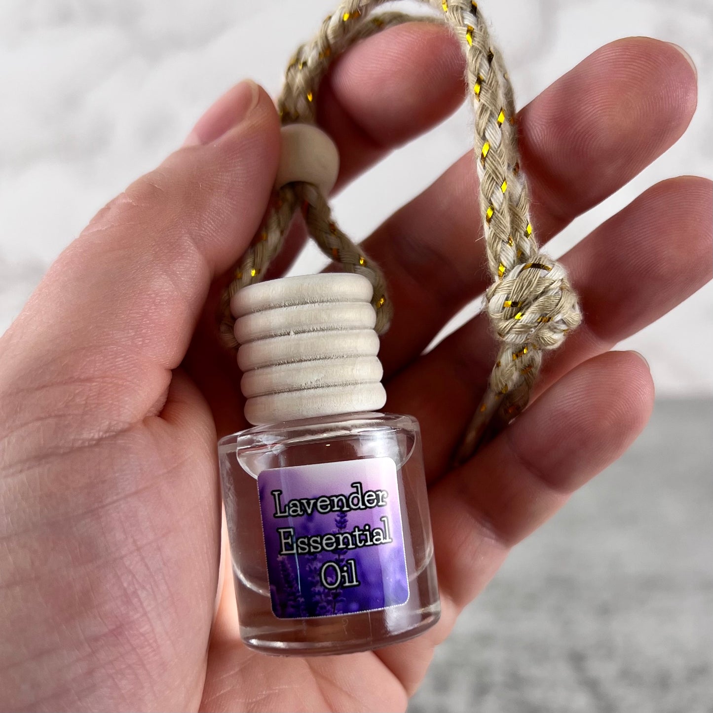 Hand holding a lavender essential oil hanging car diffuser on a neutral background.