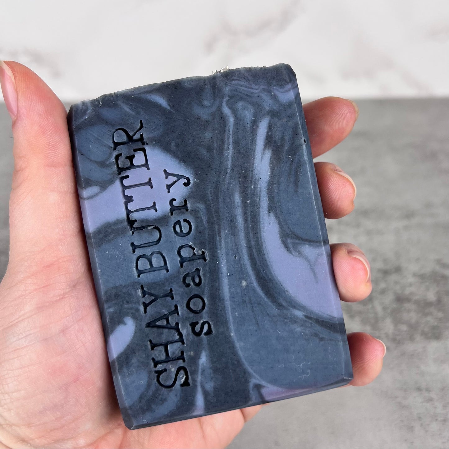 Hand holding a bar of soap with 'Shay Butter Soapery' branding.