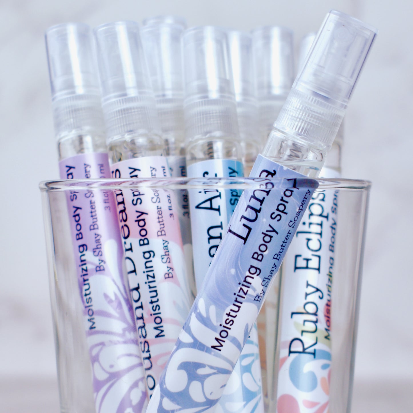 Clear spray bottles with colorful labels in a glass container on a light background