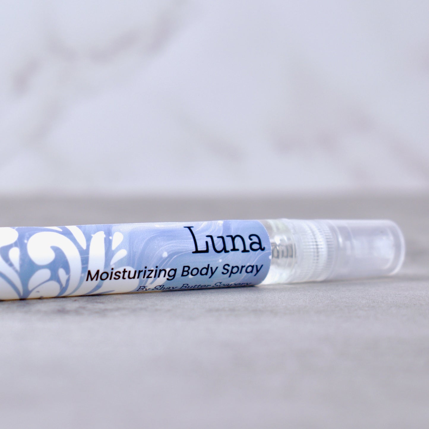 Luna moisturizing body spray on a marble surface with a light gray background