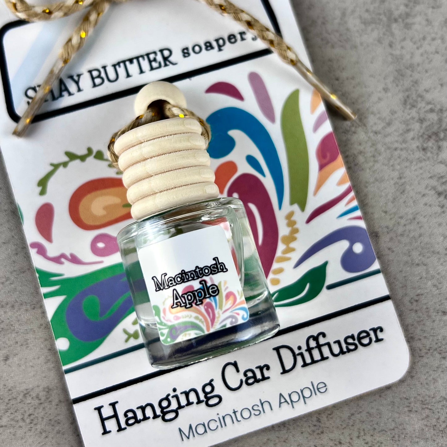 Car diffuser bottle labeled 'Macintosh Apple' on a colorful card with branding text.
