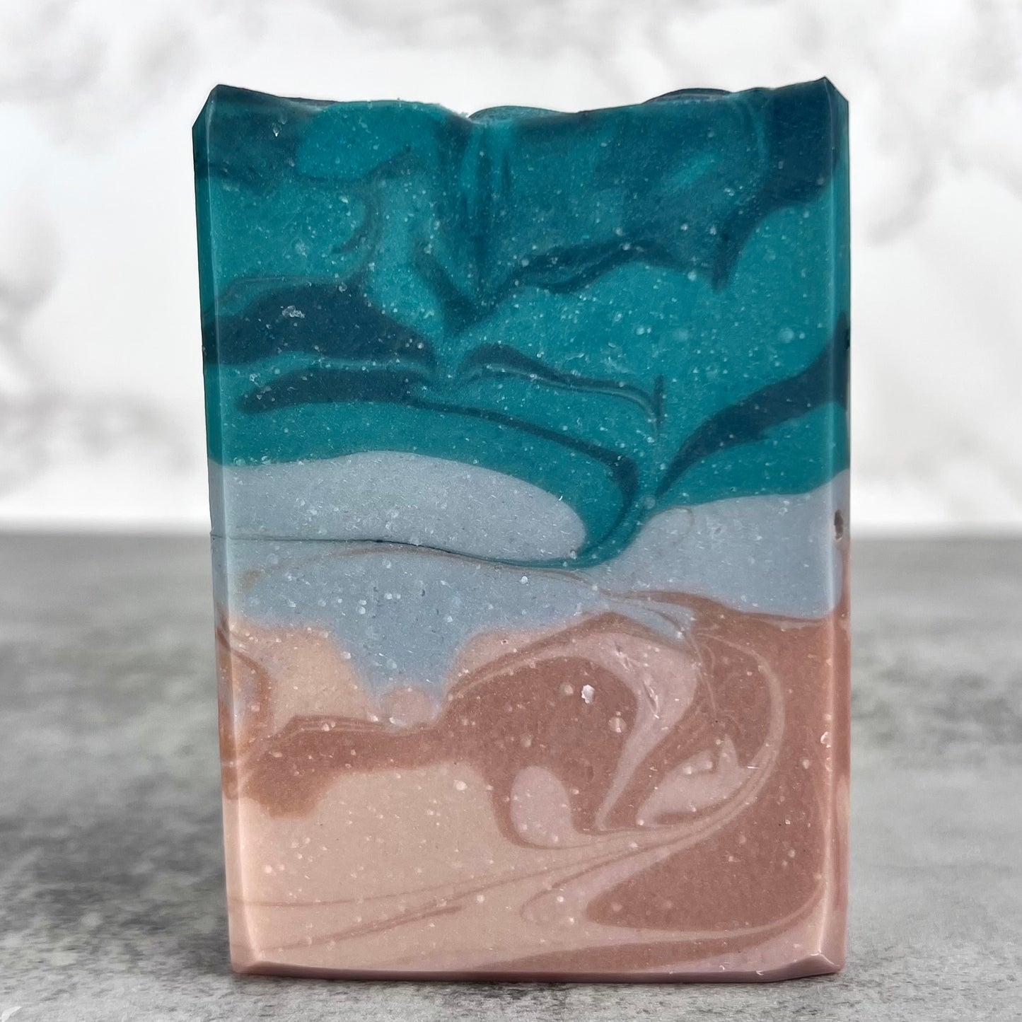 Marbled soap bar with blue, gray, and brown colors on a marble surface.