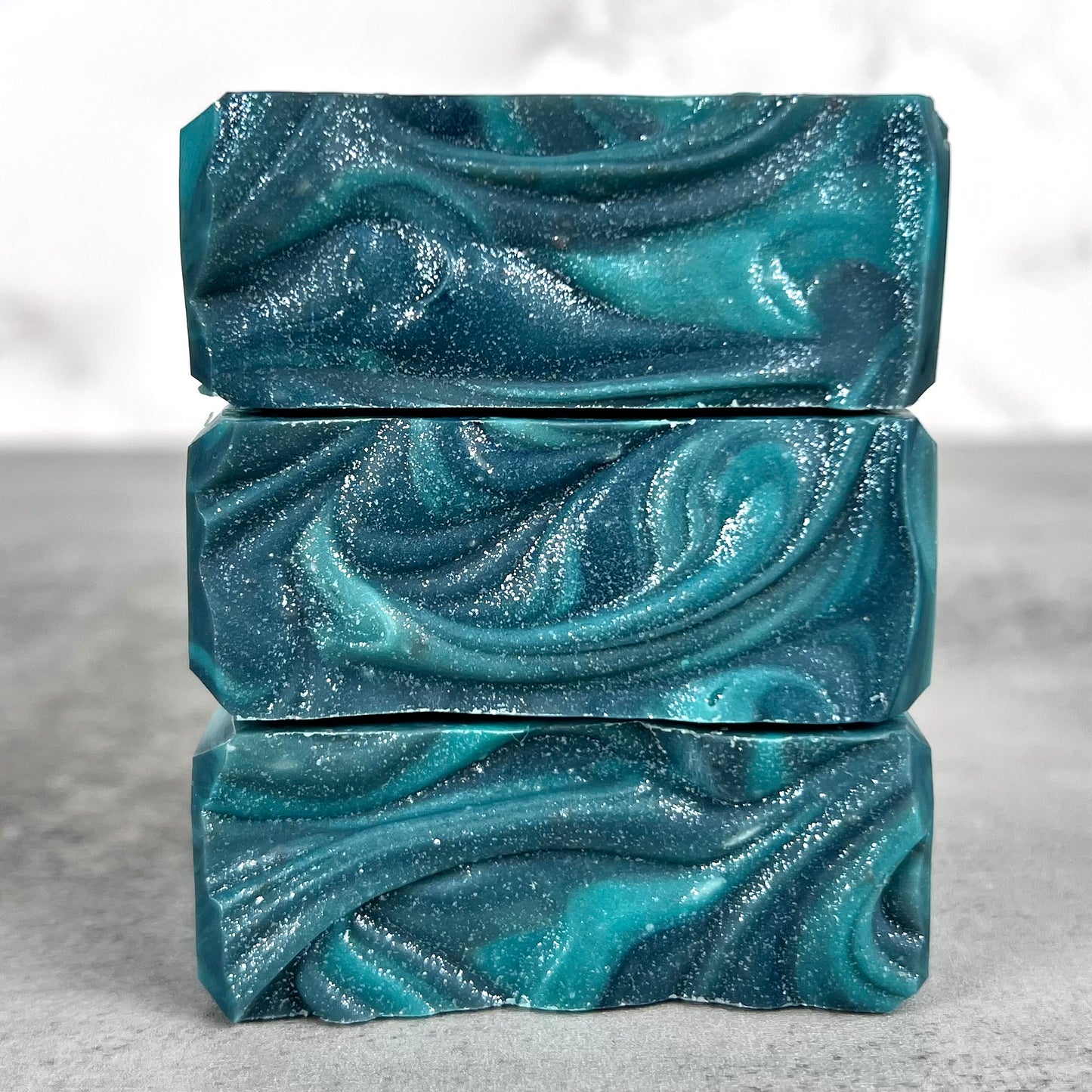 Three bars of blue marbled soap stacked on a gray surface with a light gray background