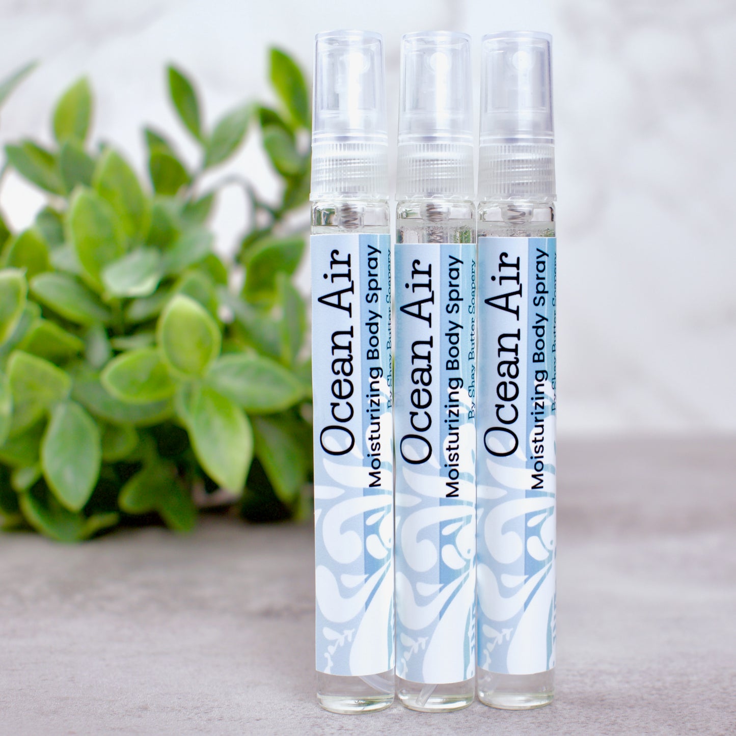 Three bottles of Ocean Air moisturizing body spray with a plant in the background.