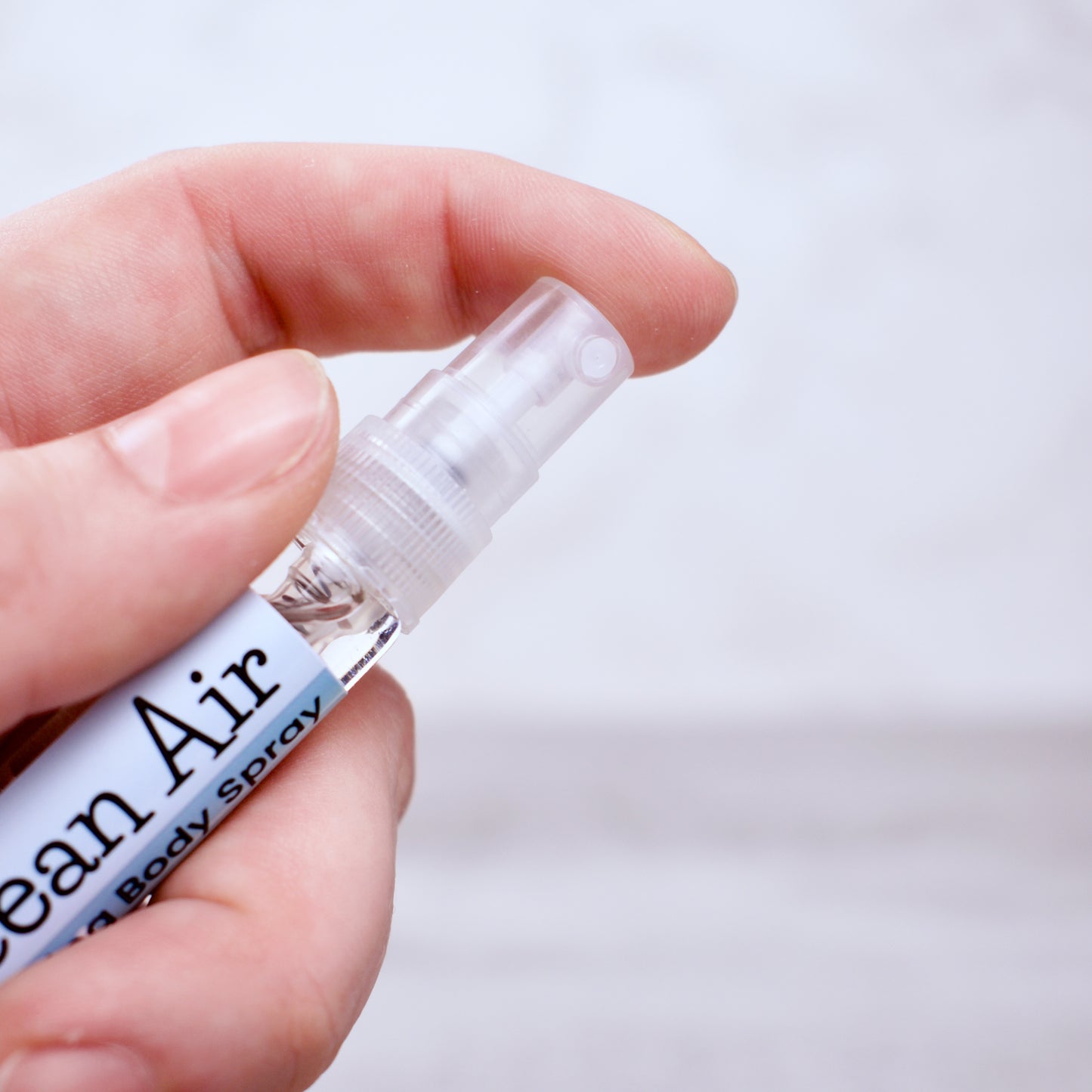 Hand holding a small spray bottle labeled 'Ocean Air' against a light background