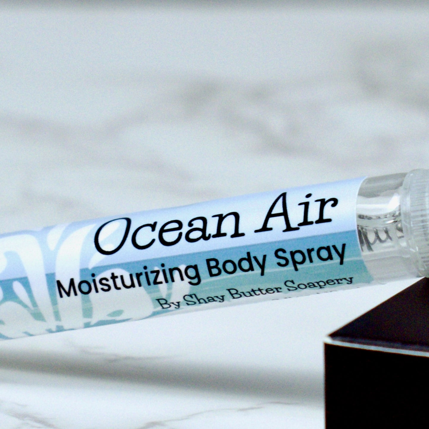 Body spray labeled 'Ocean Air' by Shay Butter Soapery on a marble surface.