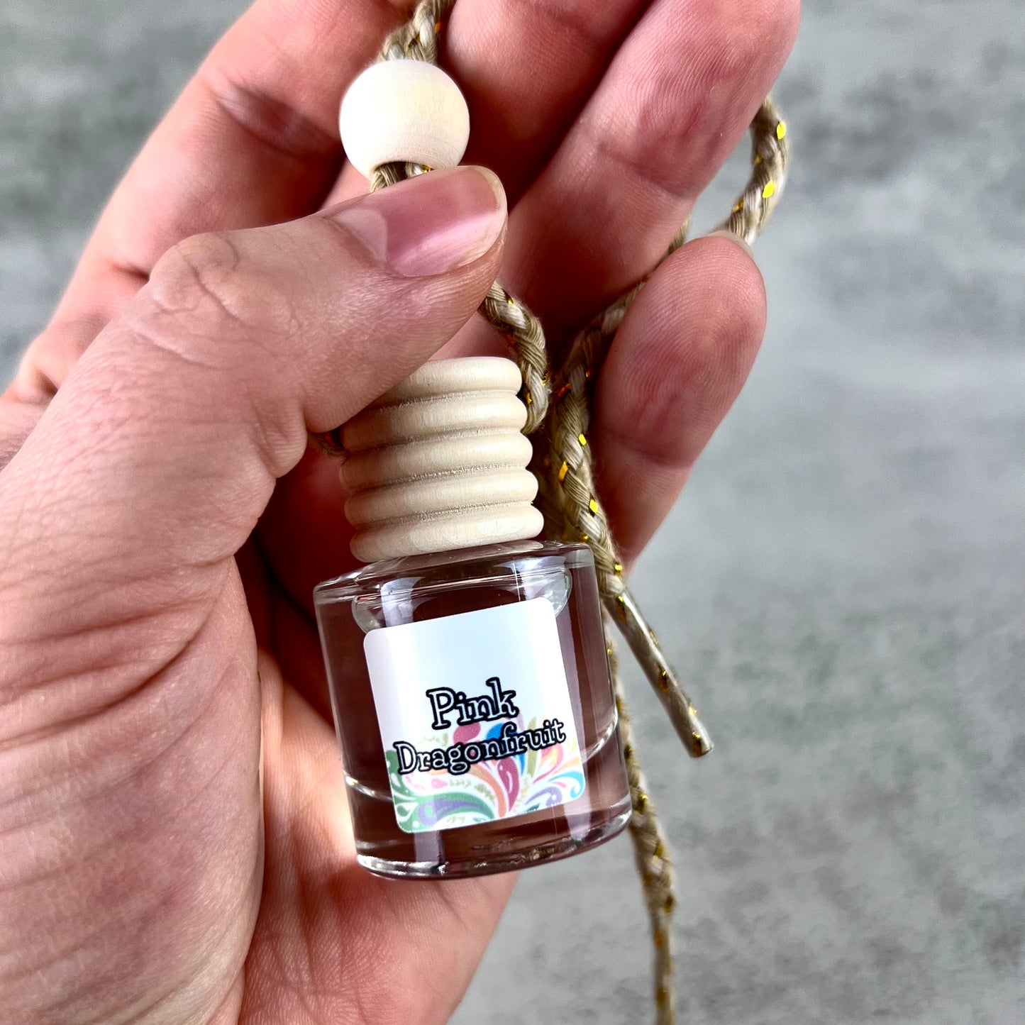 Car diffuser labeled 'Pink Dragonfruit' held in a hand with a blurred background