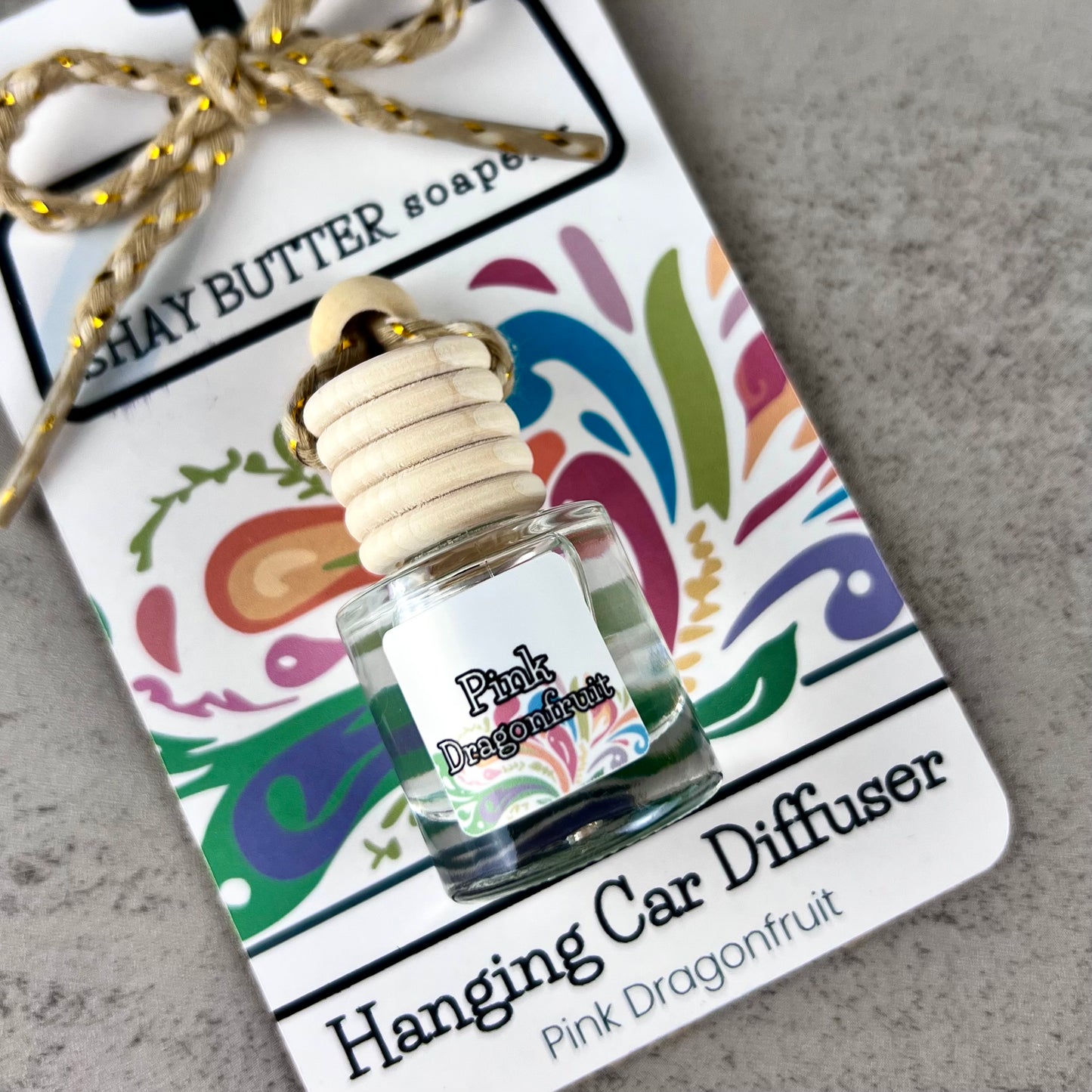Pink Dragonfruit hanging car diffuser with decorative label on a gray surface