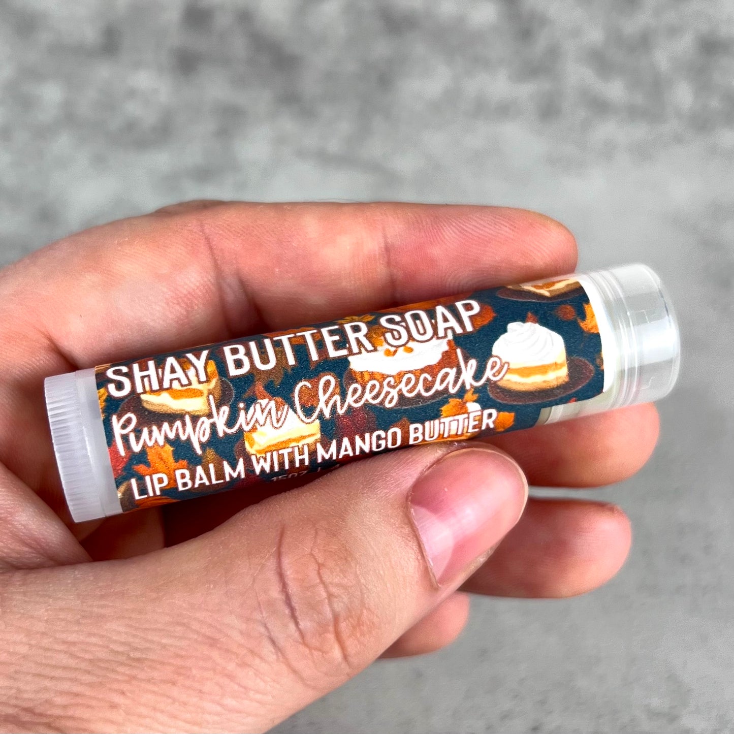 Lip balm with 'Shay Butter Soap' packaging held in a hand against a gray background