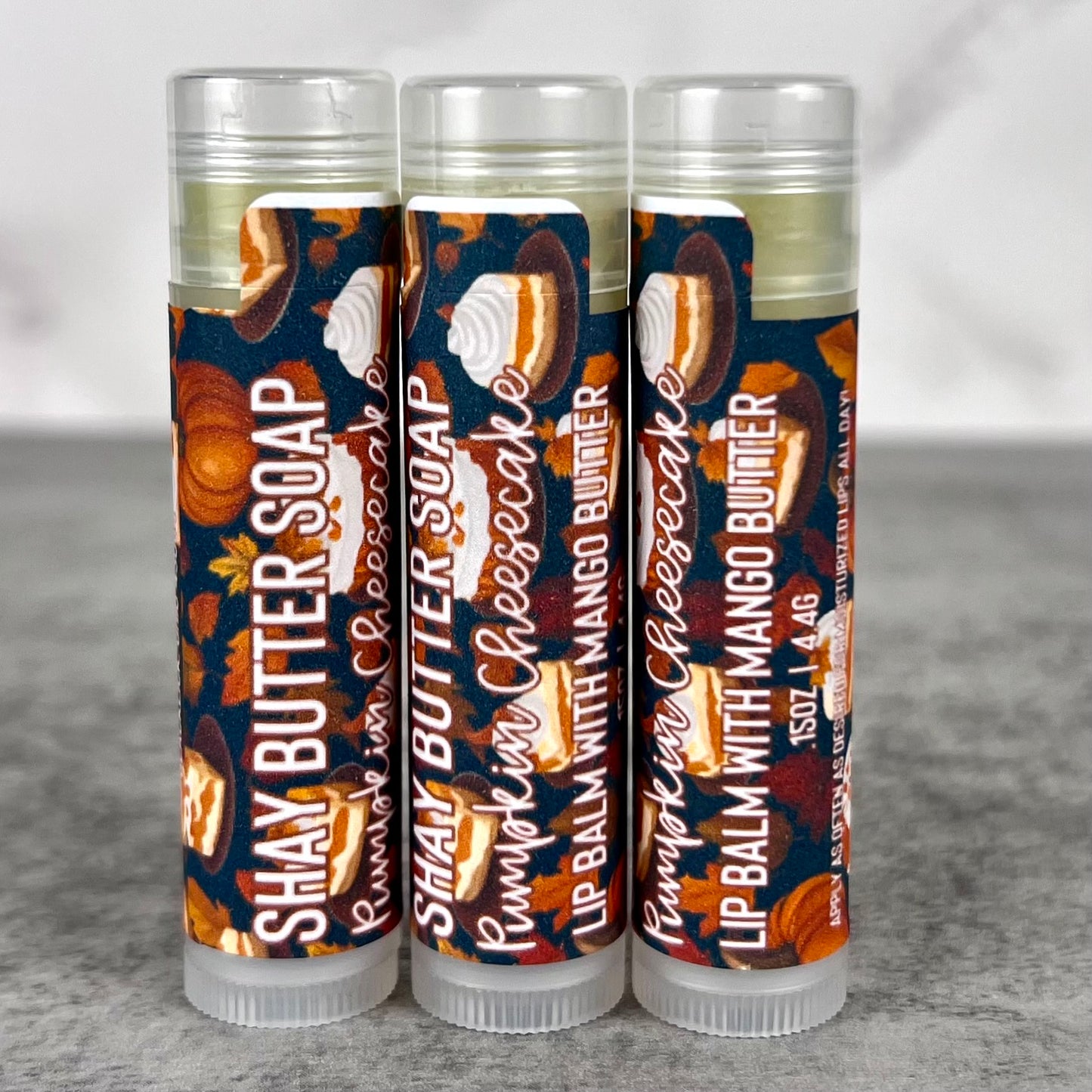 Three lip balm tubes with colorful packaging on a gray surface.