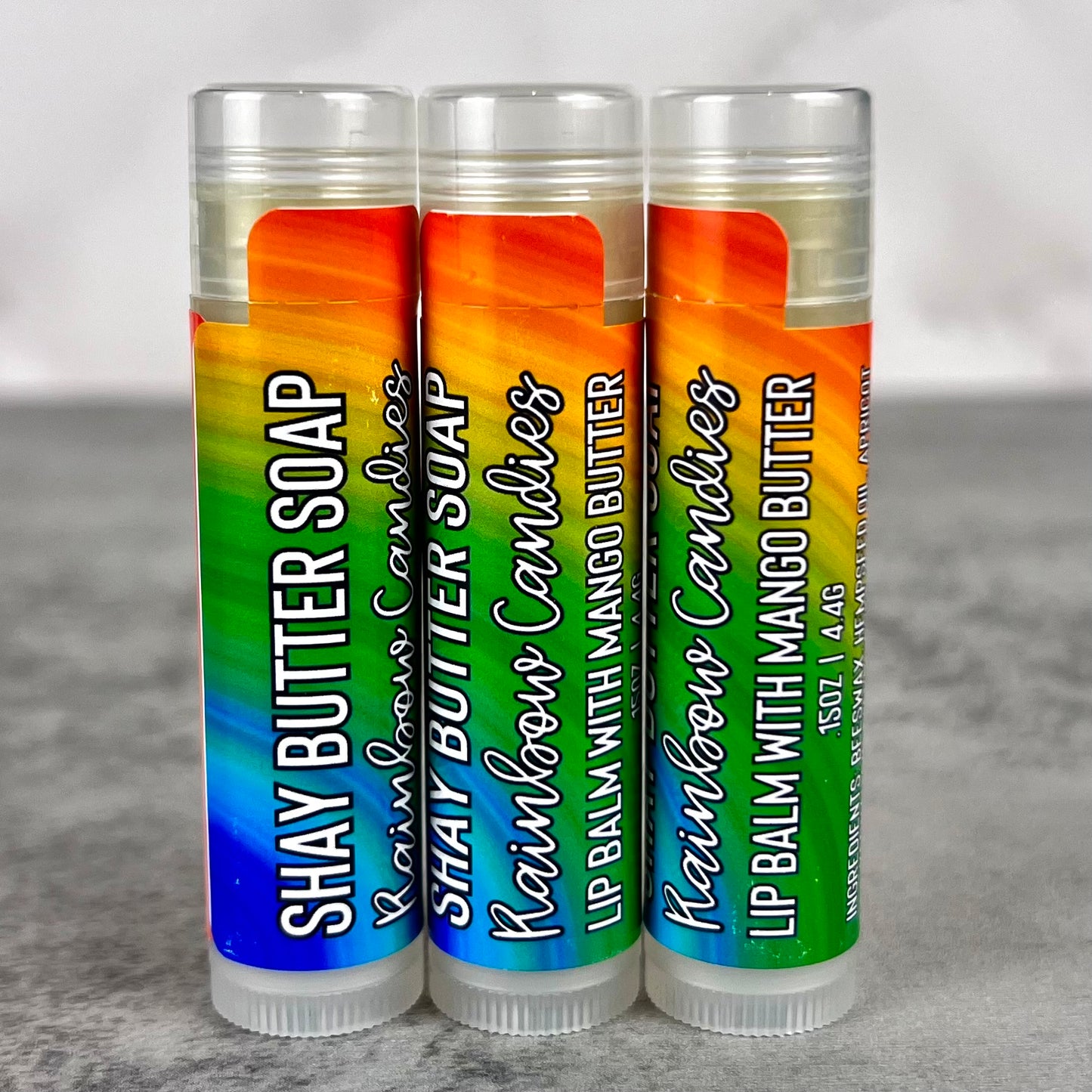 Three lip balms with colorful packaging on a gray surface.
