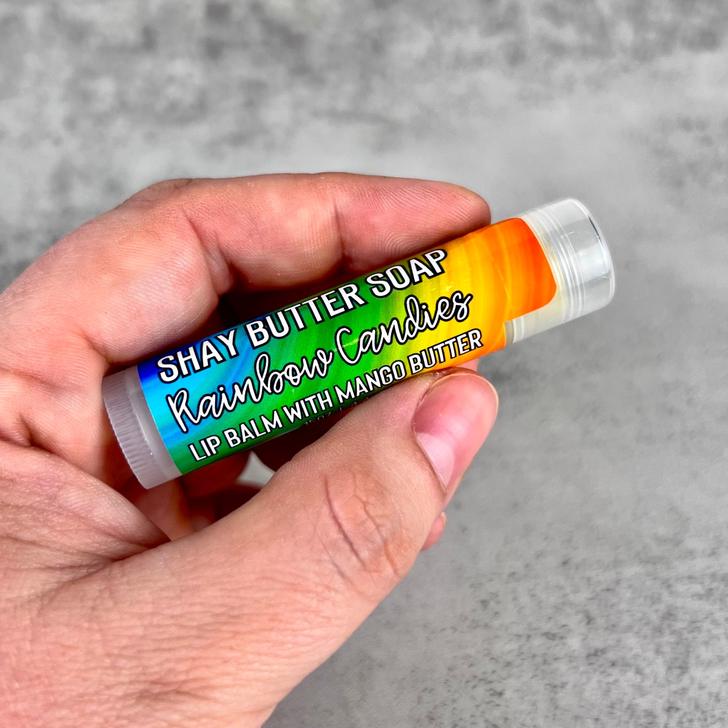 Hand holding a lip balm with colorful packaging against a gray background