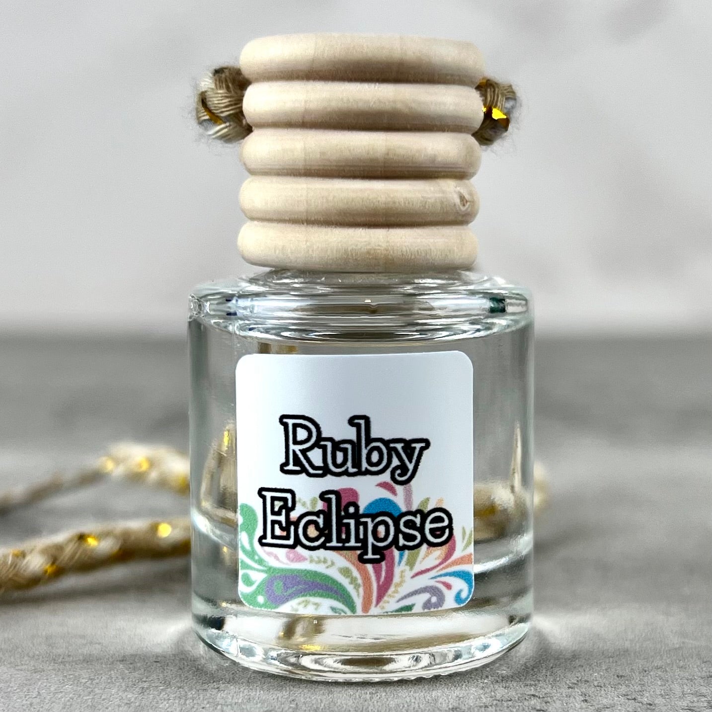 Hanging car diffuser labeled 'Ruby Eclipse' with wooden elements on a neutral background