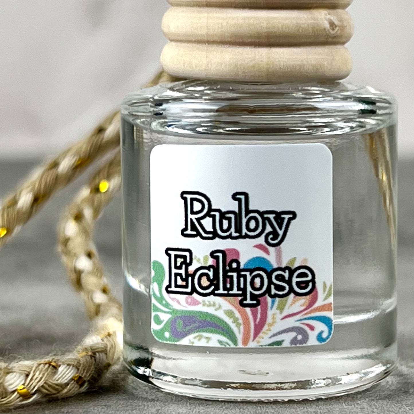 Up close photo of a hanging car diffuser with "Ruby Eclipse" label on grey background.