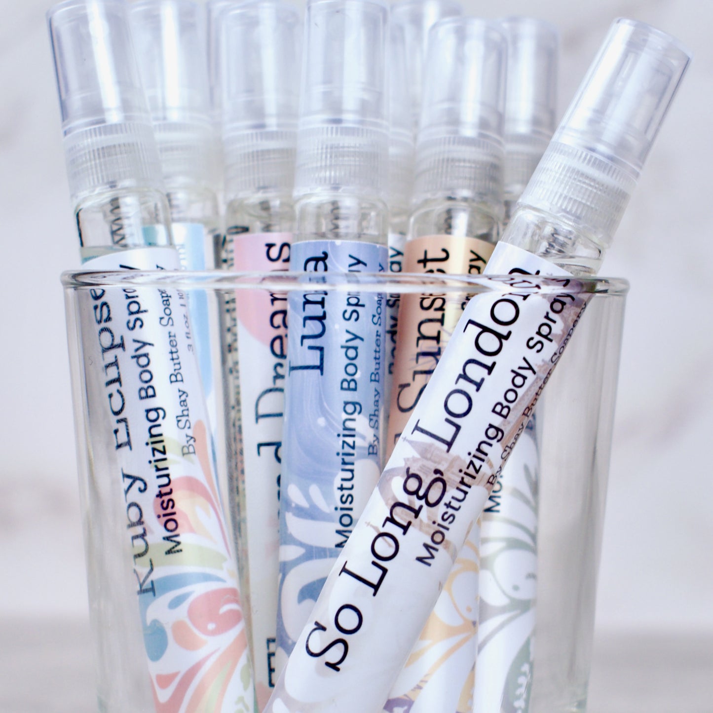 several bottles of body sprays in a clear glass with colorful labels