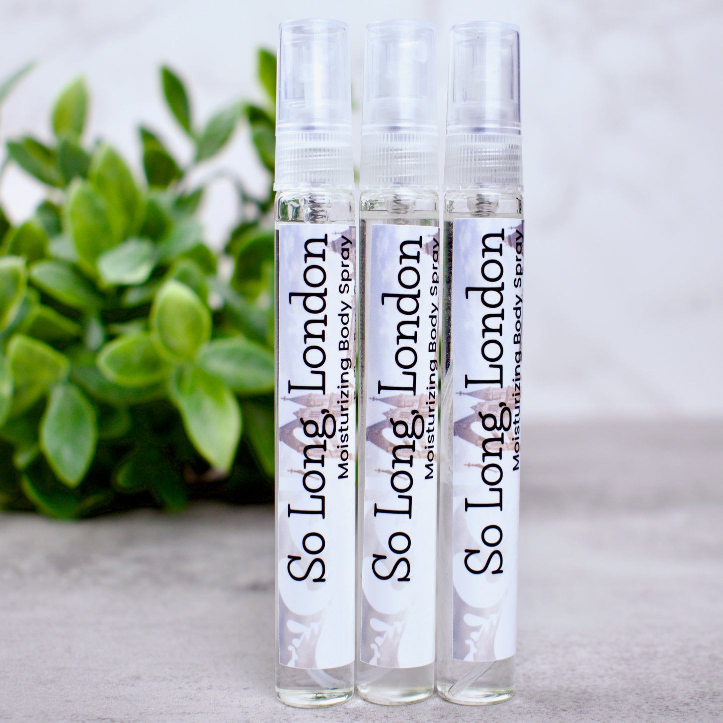 three bottles of body spray on grey background with greenery