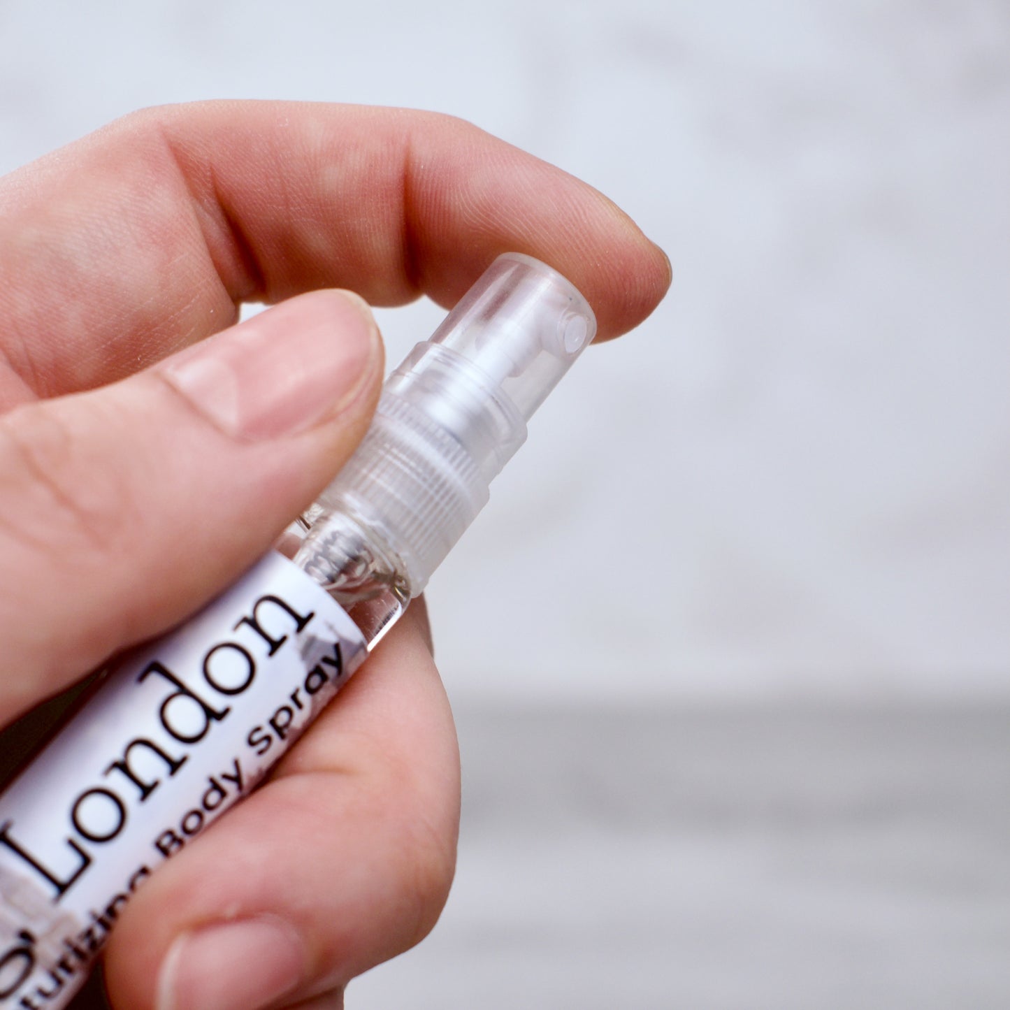 a hand holding a bottle of "so long, london" body spray on a neutral bakground