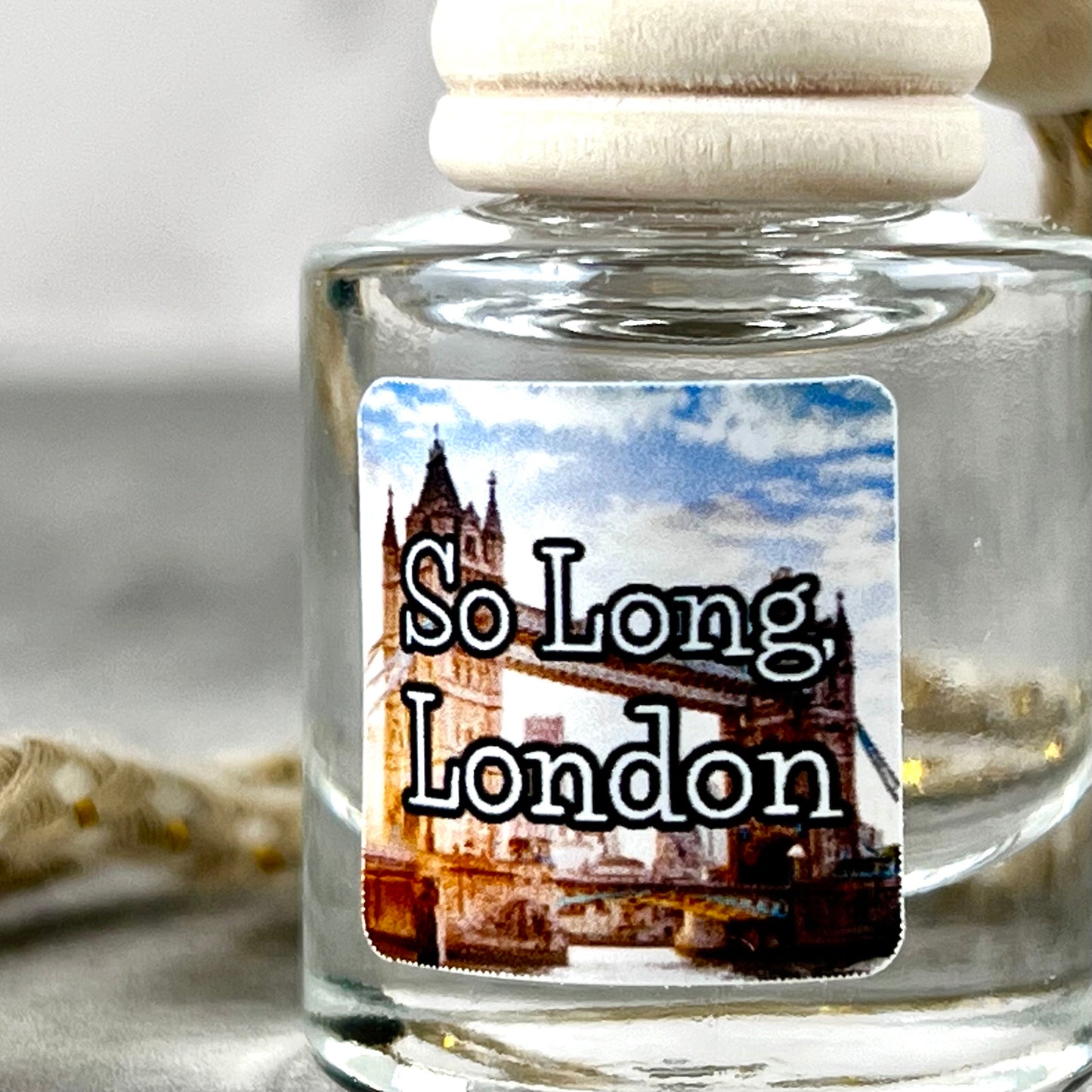Up close photo of hanging car diffuser with "So Long, London" label on grey background.