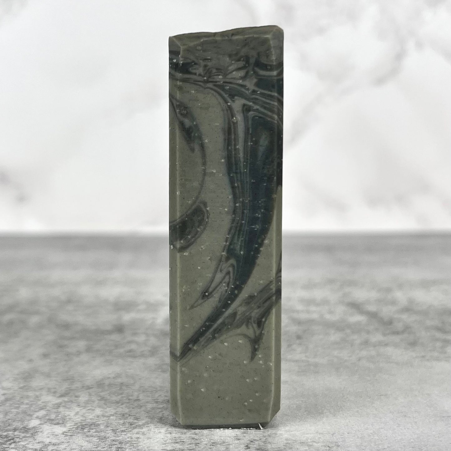 Marbled gray and black soap bar on a textured surface with a light gray background