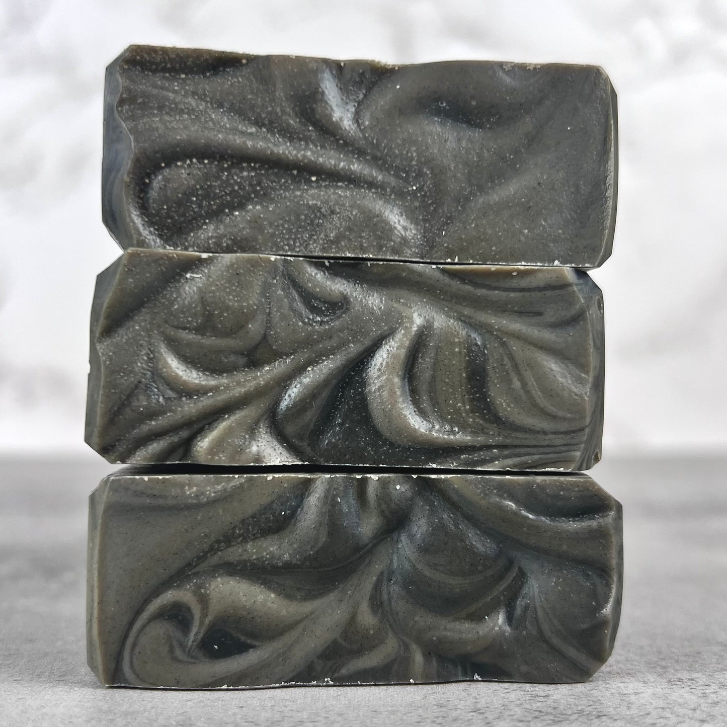 Three bars of dark gray soap with a textured surface on a light gray background