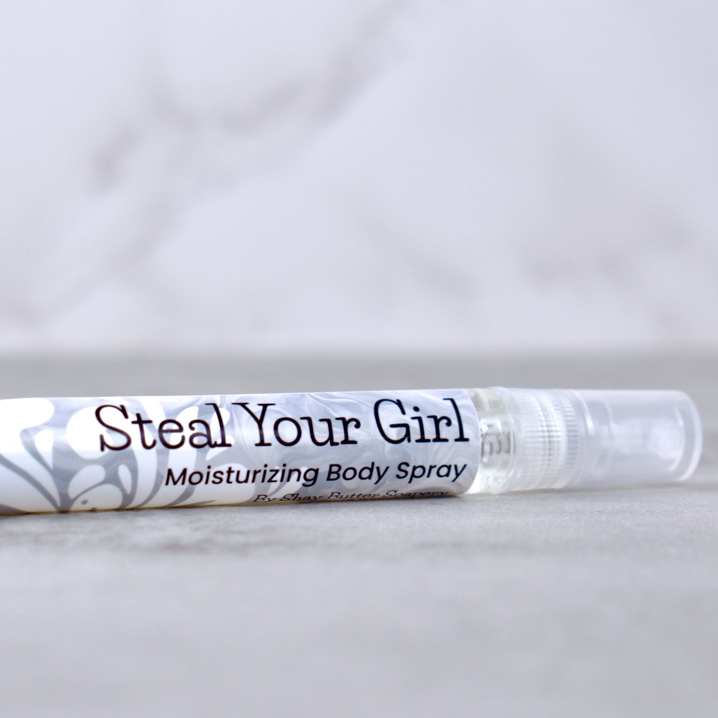 Moisturizing body spray labeled 'Steal Your Girl' on a marble surface with a light gray background