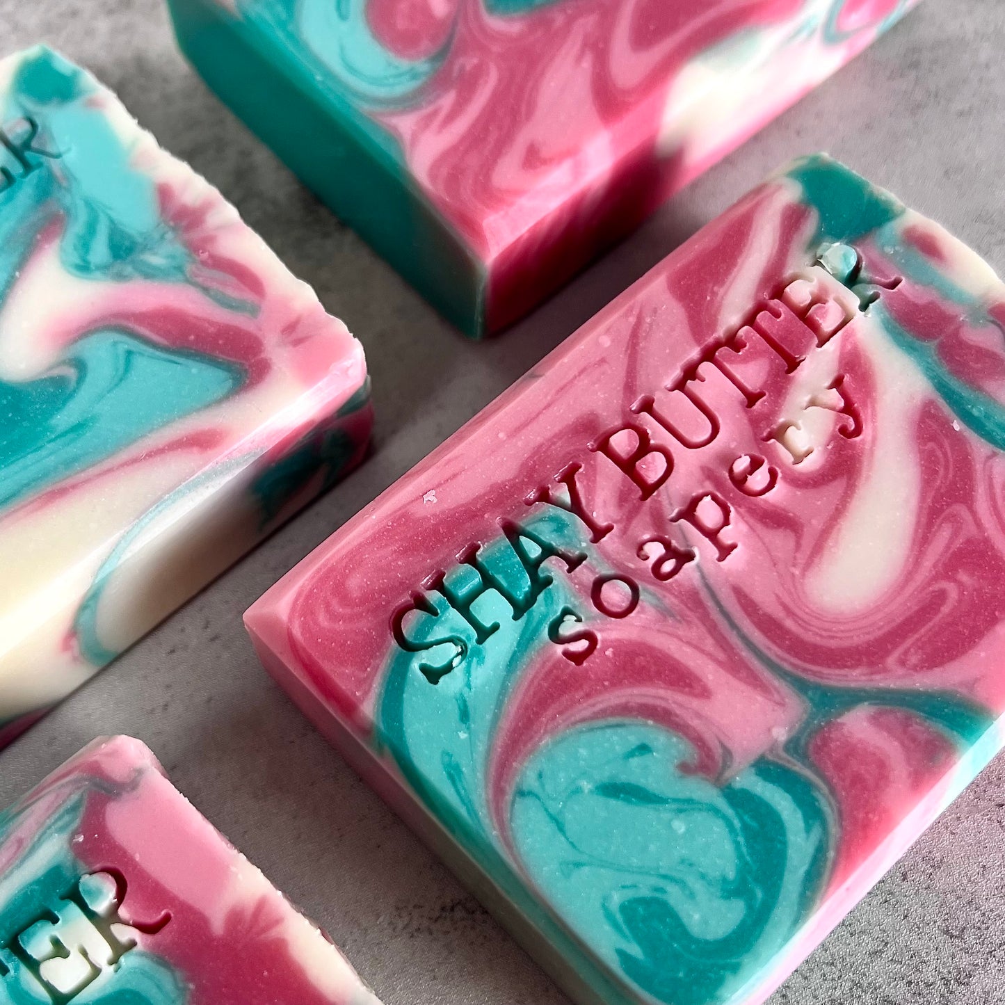 Marbled pink and blue soap bars with 'Shay Butter Soapery' branding on a gray surface.