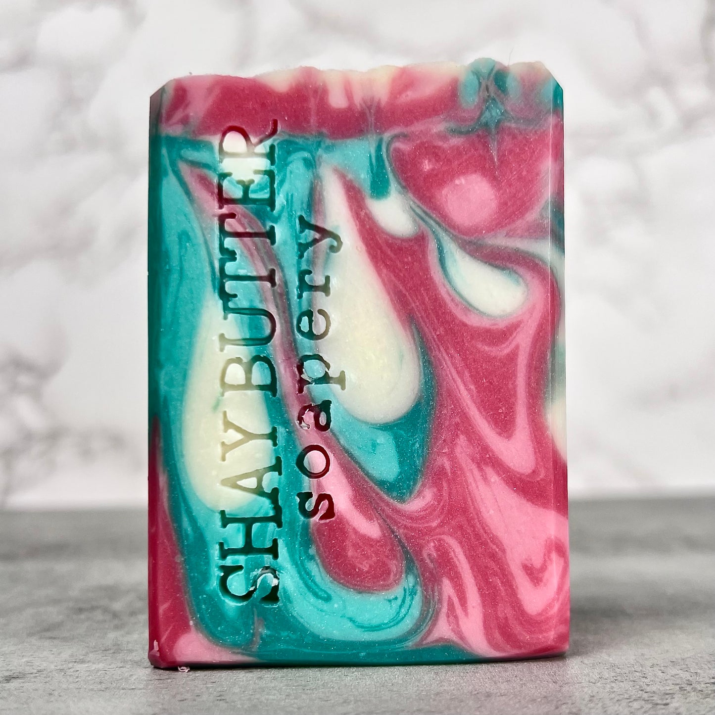 Marbled pink and blue soap bar with 'Shay Butter Soapery' branding on a gray background