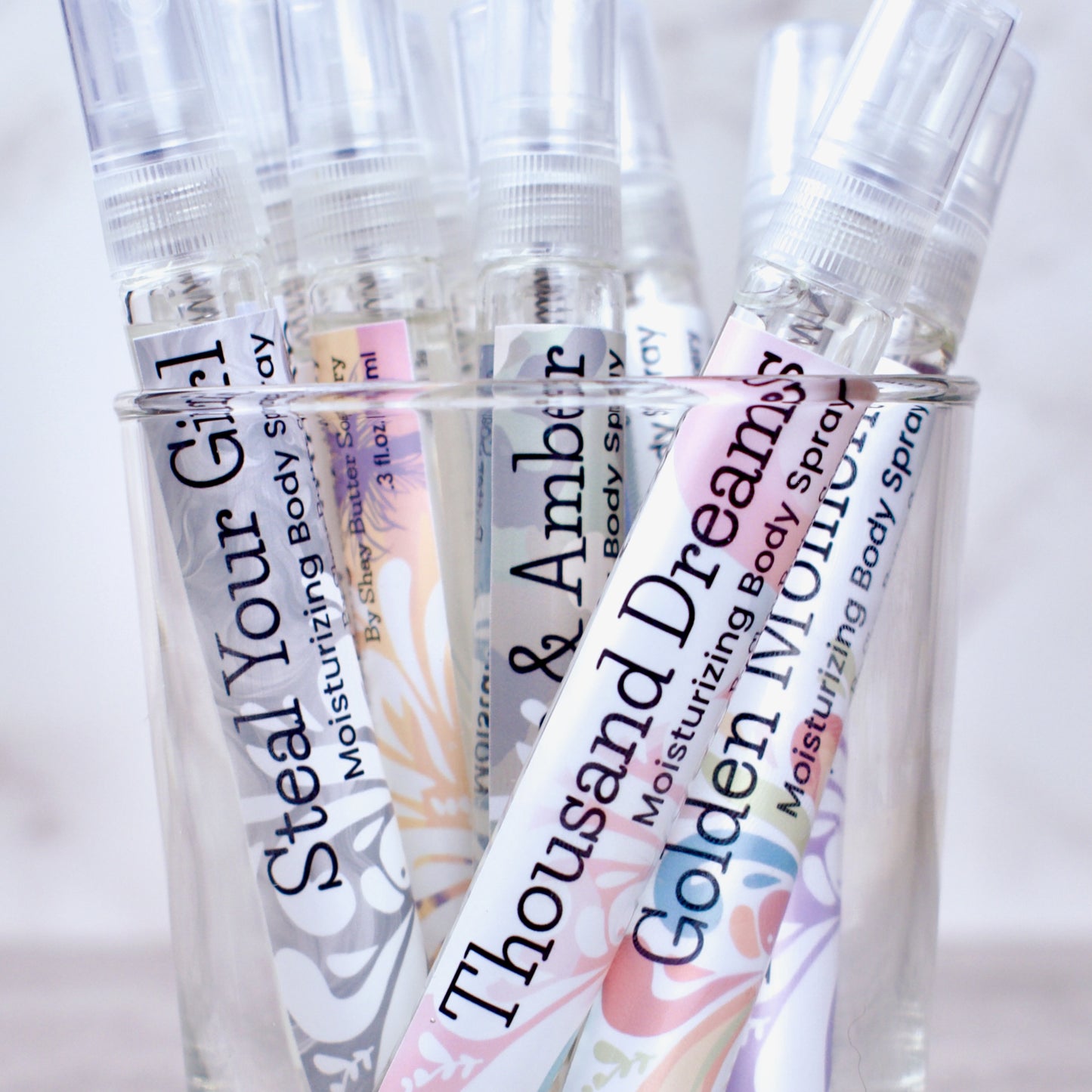 Collection of moisturizing body spray bottles with colorful labels on a light background