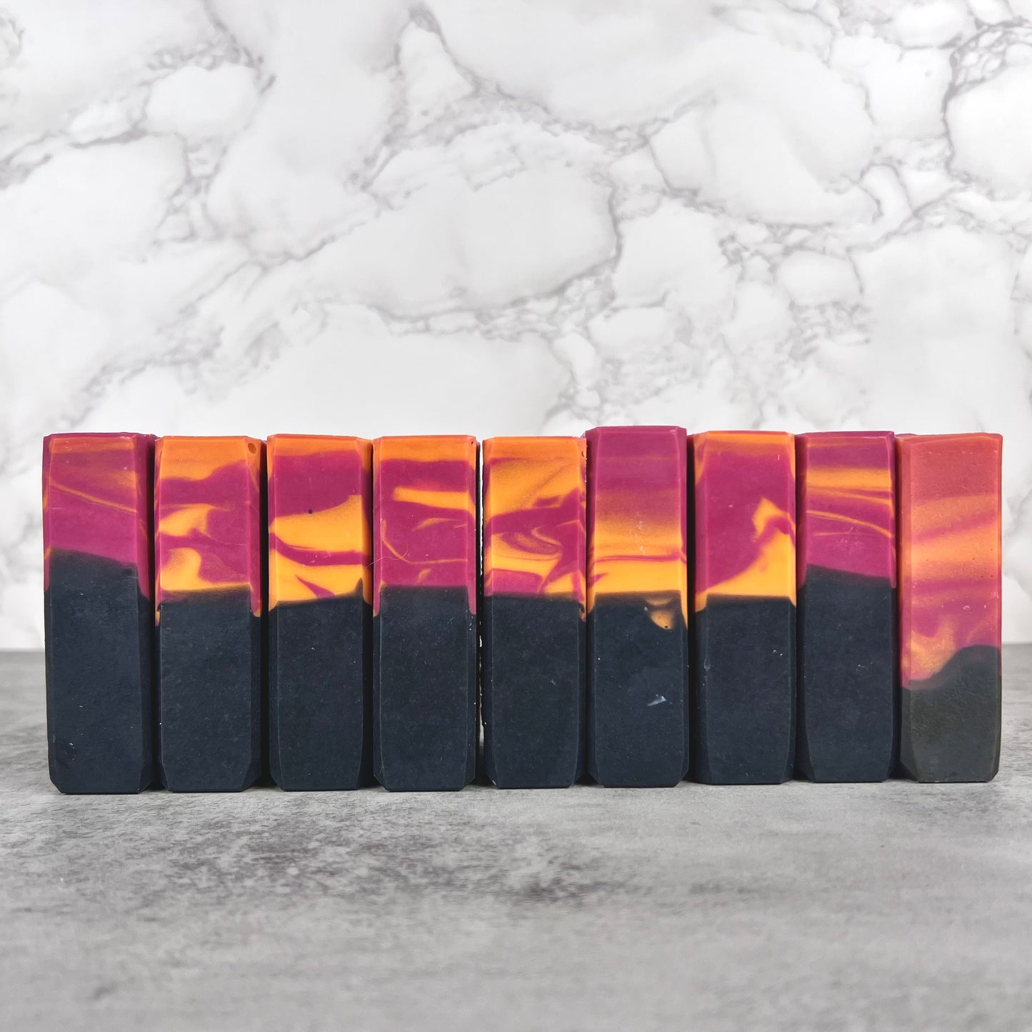 Row of marbled soap bars with black, orange, and purple colors on a marble background